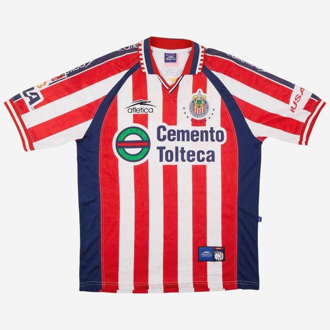 The Retro1999 Chivas 1999-00 Home Shirt features red and white vertical stripes, blue side panels, and classic Atlética, Cemento Tolteca, and Chivas crest logos—a faithful tribute to a legendary kit in soccer history.