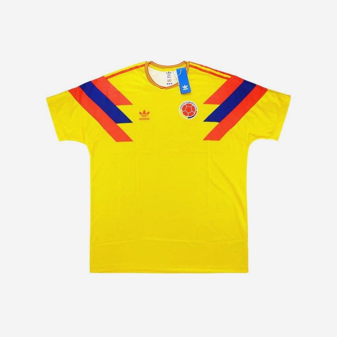 The Colombia 1990 Home Shirt by Retro1999 features yellow fabric with red and blue shoulder stripes, the team badge on the left chest, and a blue tag at the collar—a true classic for fans.