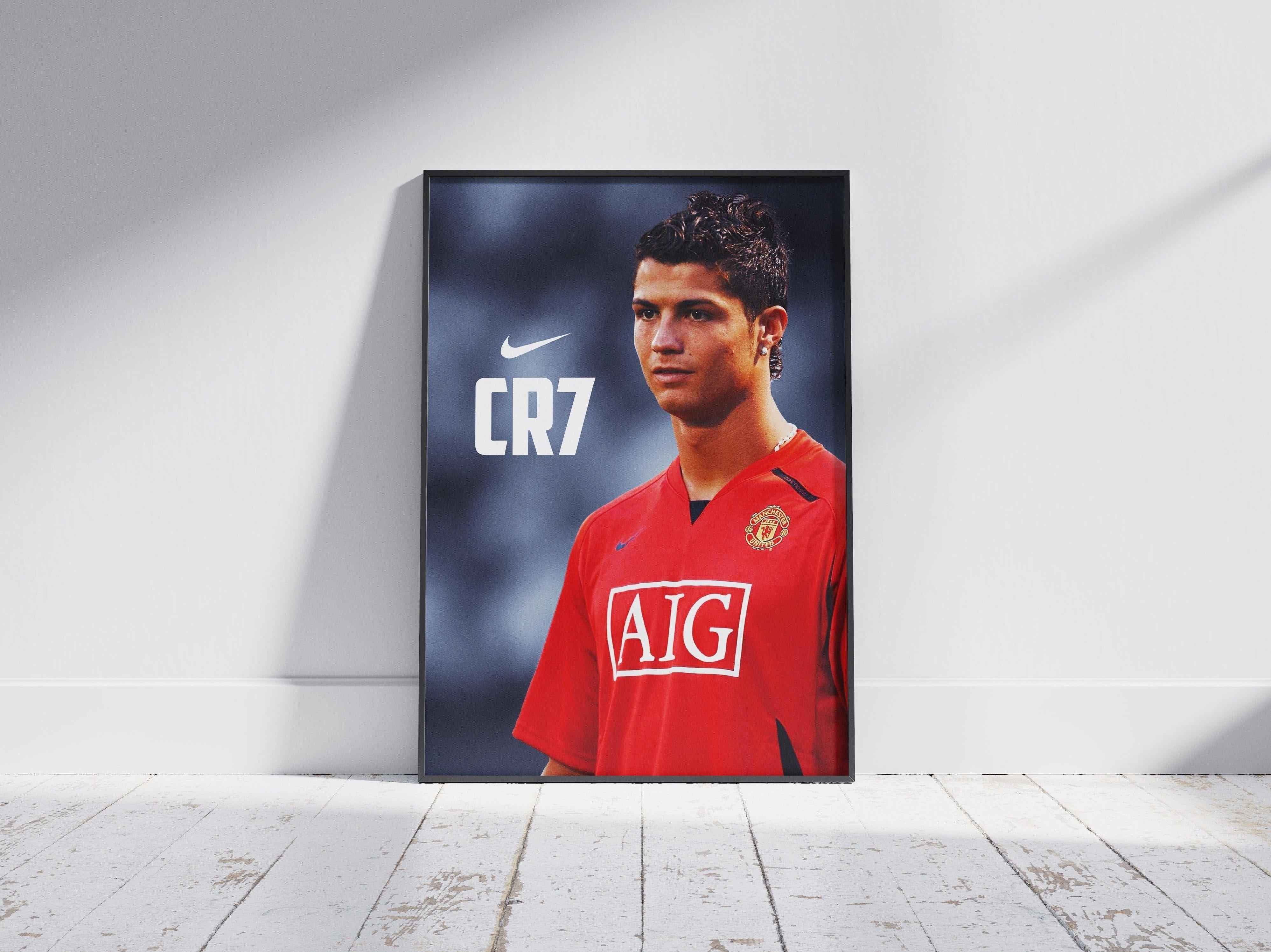 The Retro1999 CR7 Manchester United Poster features Cristiano Ronaldo in a red jersey with AIG sponsor and Nike logo, framed and displayed on a wooden floor, making it an eye-catching piece of football memorabilia.