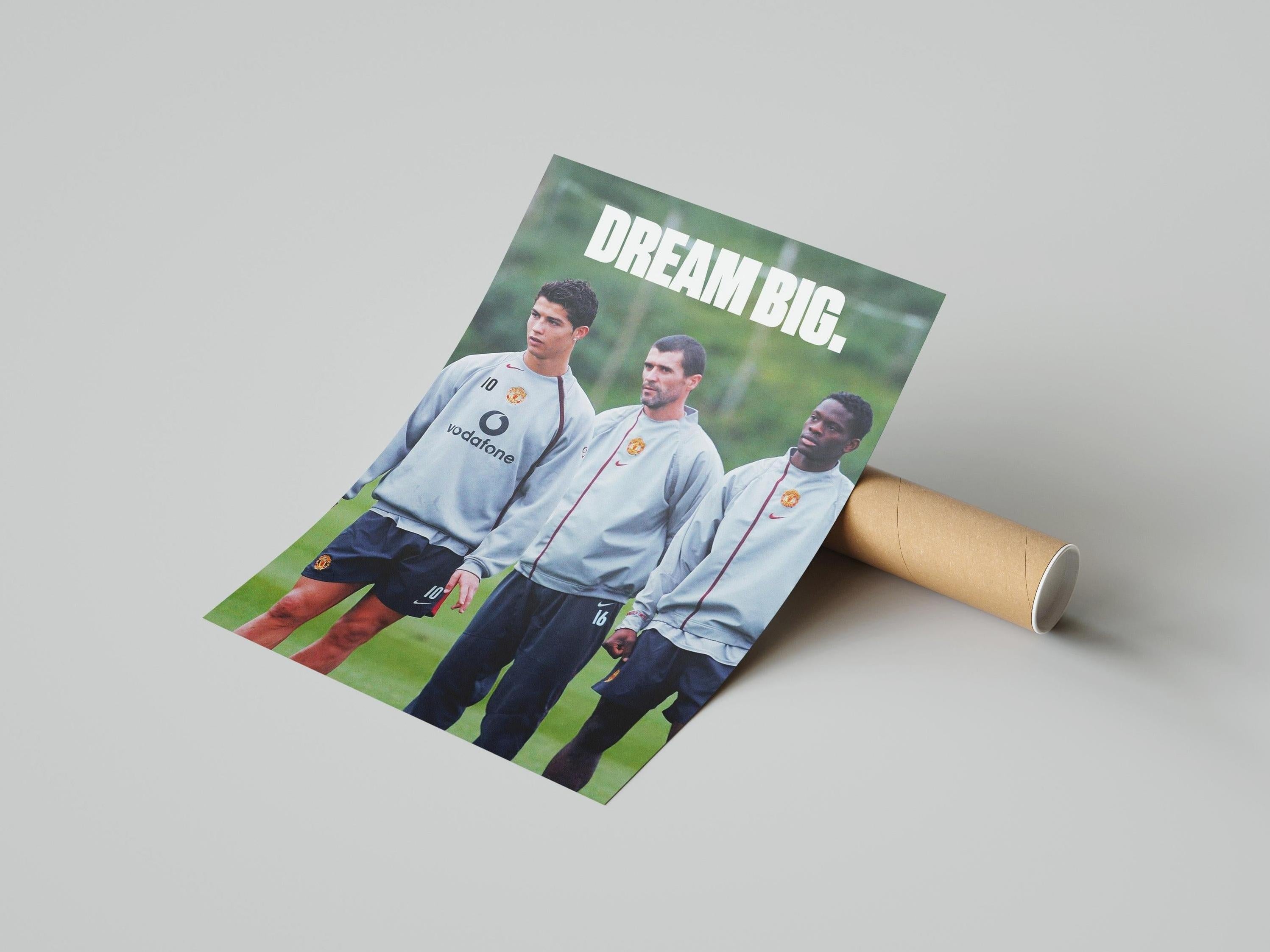 The Retro1999 Cristiano Ronaldo Dream Big Poster features three Manchester United players in training gear on a field with DREAM BIG. above them—the perfect wall art for football fans. The high-quality print comes partially rolled beside a cardboard tube.