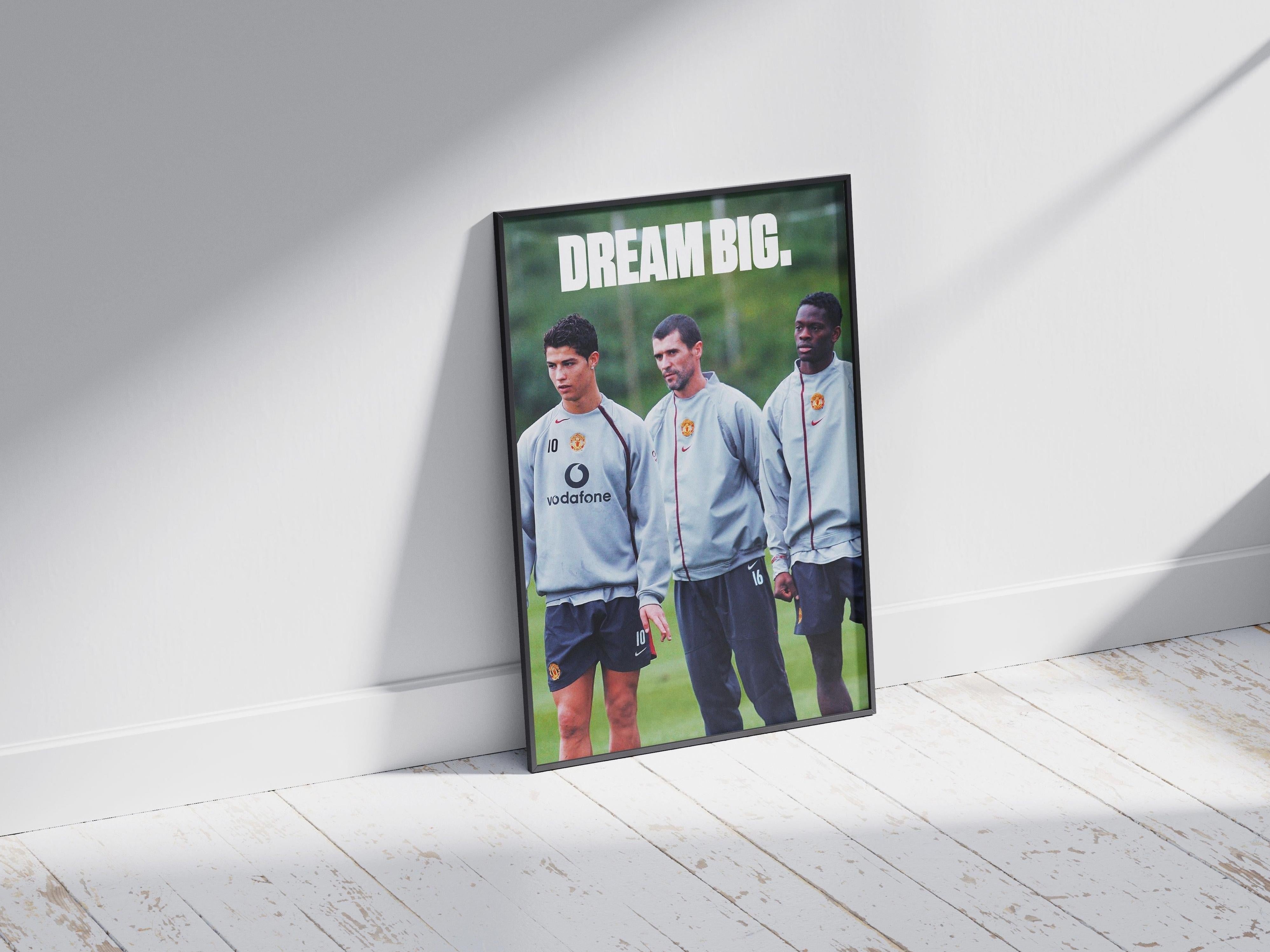 The Cristiano Ronaldo Dream Big Poster by Retro1999 features three footballers in gray Manchester United training kits under bold white text, framed on a light wooden floor with sunlit shadows—an ideal piece for football fans.