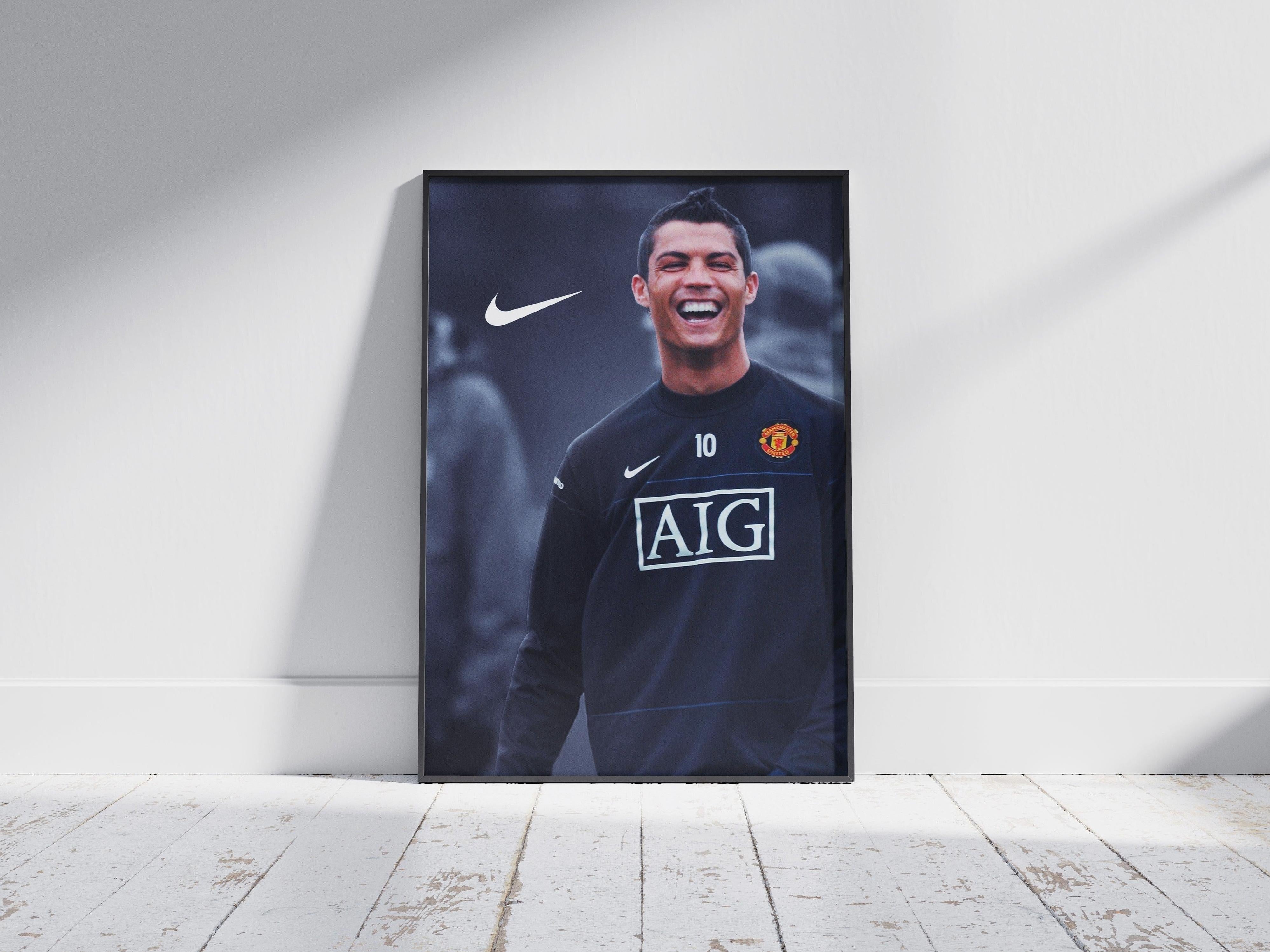 Retro1999 Cristiano Ronaldo Manchester United Poster—framed wall art displays Ronaldo in a black kit with AIG sponsor and Nike logo, shown on a white wooden floor against a white wall; perfect décor for football fans.