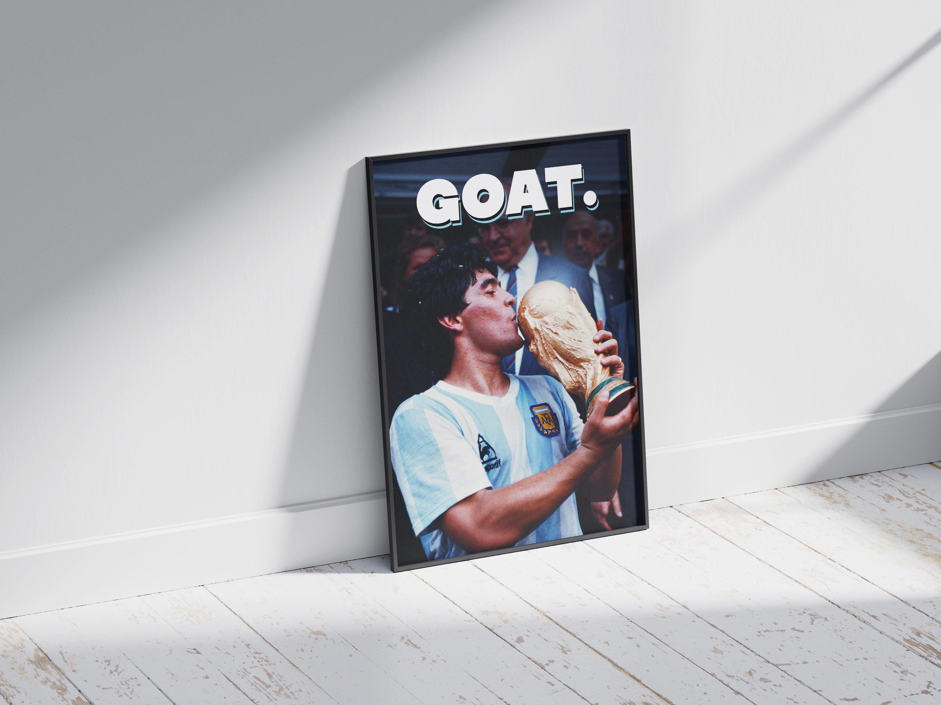 The Retro1999 Diego Maradona GOAT Poster features Maradona in an Argentina jersey kissing the 1986 FIFA World Cup trophy, with “GOAT.” above—framed and displayed against a white wall on a sunlit wooden floor.