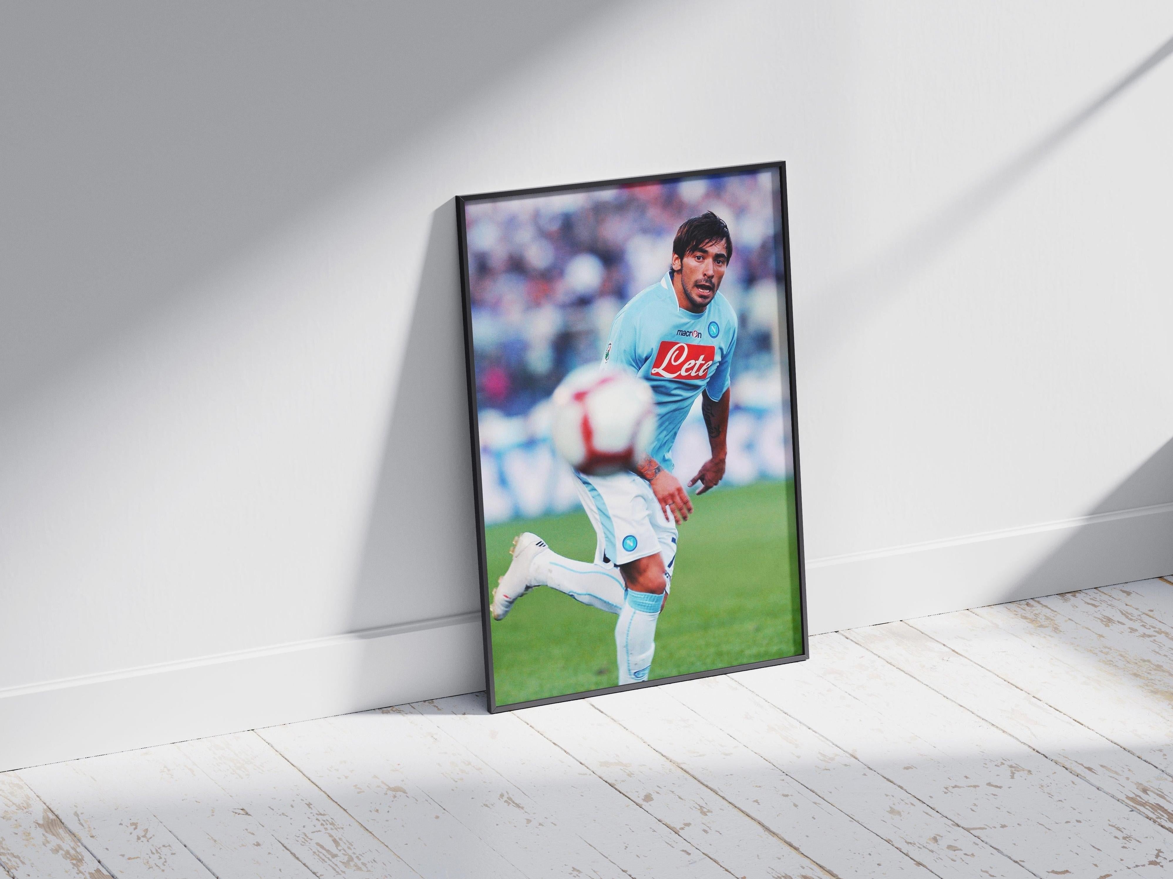 The Retro1999 Ezequiel Lavezzi x SSC Napoli Poster features the star in a light blue uniform sprinting during a Serie A match, displayed on a white wooden floor and leaning against a white wall with sunlight and shadows.