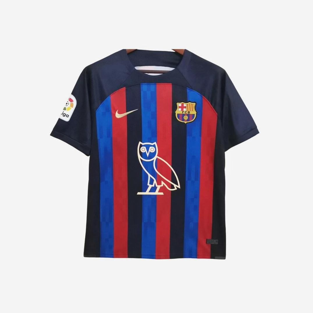 The FC Barcelona x Drake - OVO Limited Edition 2022-23 Home Shirt by Retro1999 features dark blue and red stripes, Nike logo, club crest, La Liga sleeve patch, and a bold white owl graphic—a standout La Liga collectible.