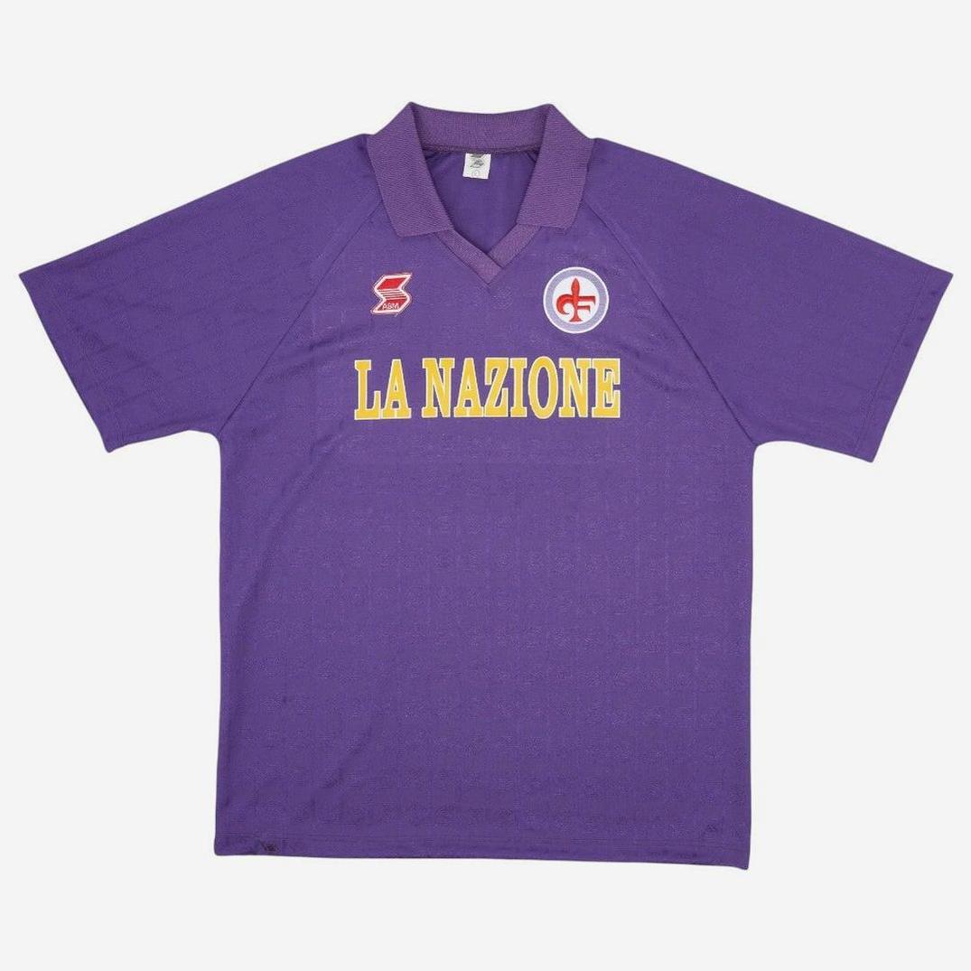 The Retro1999 Fiorentina 1989-90 Home Shirt is a purple retro soccer jersey with yellow LA NAZIONE text, a red and white badge on the left chest, and a red logo on the right—echoing the classic Serie A kit.