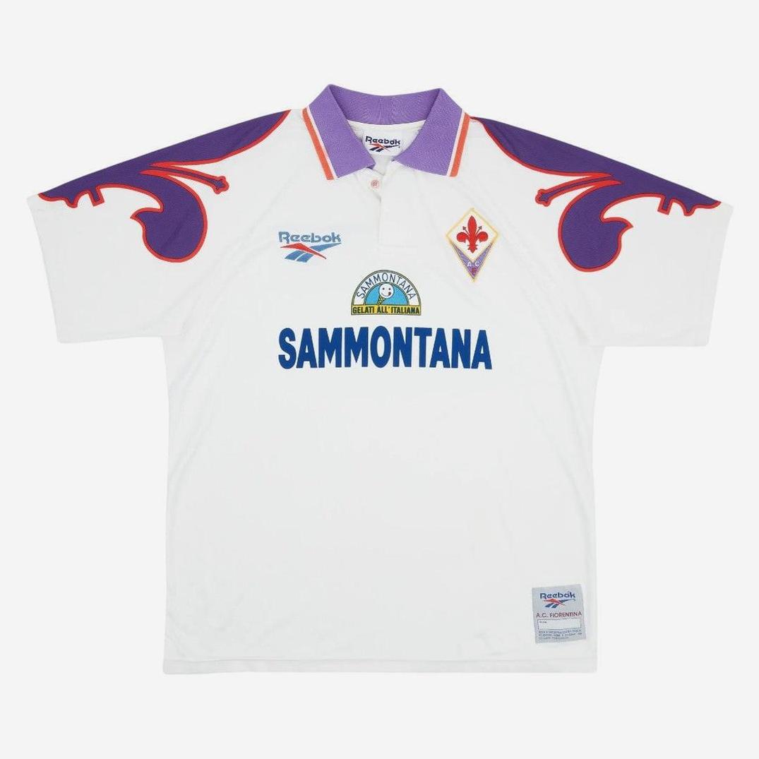 The Retro1999 Fiorentina 1995-96 Away Shirt is a white retro kit with a purple collar, red and purple shoulder accents, club badge, Reebok logo, and Sammontana sponsor—an iconic look from the Serie A era.