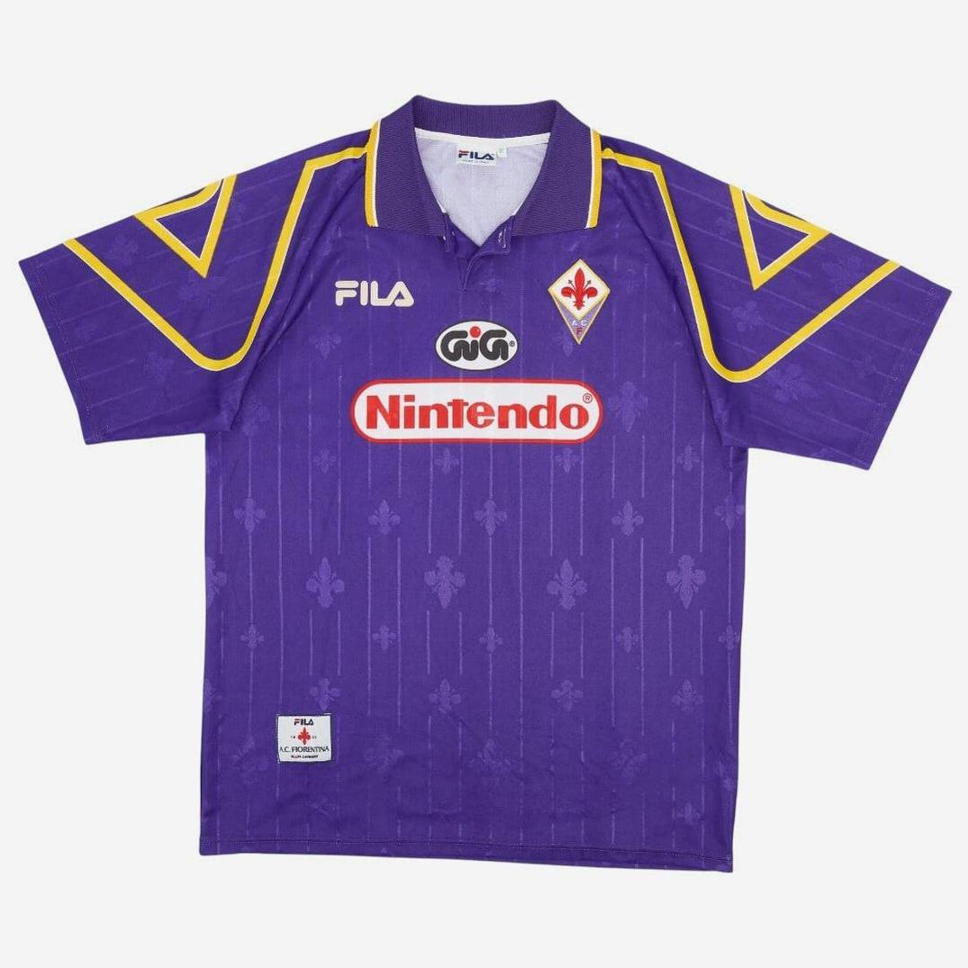 The Fiorentina 1997-98 Home Shirt by Retro1999 features purple with yellow accents, FILA and Nintendo logos, the club crest, and fleur-de-lis patterns—a must-have retro kit for Serie A fans.