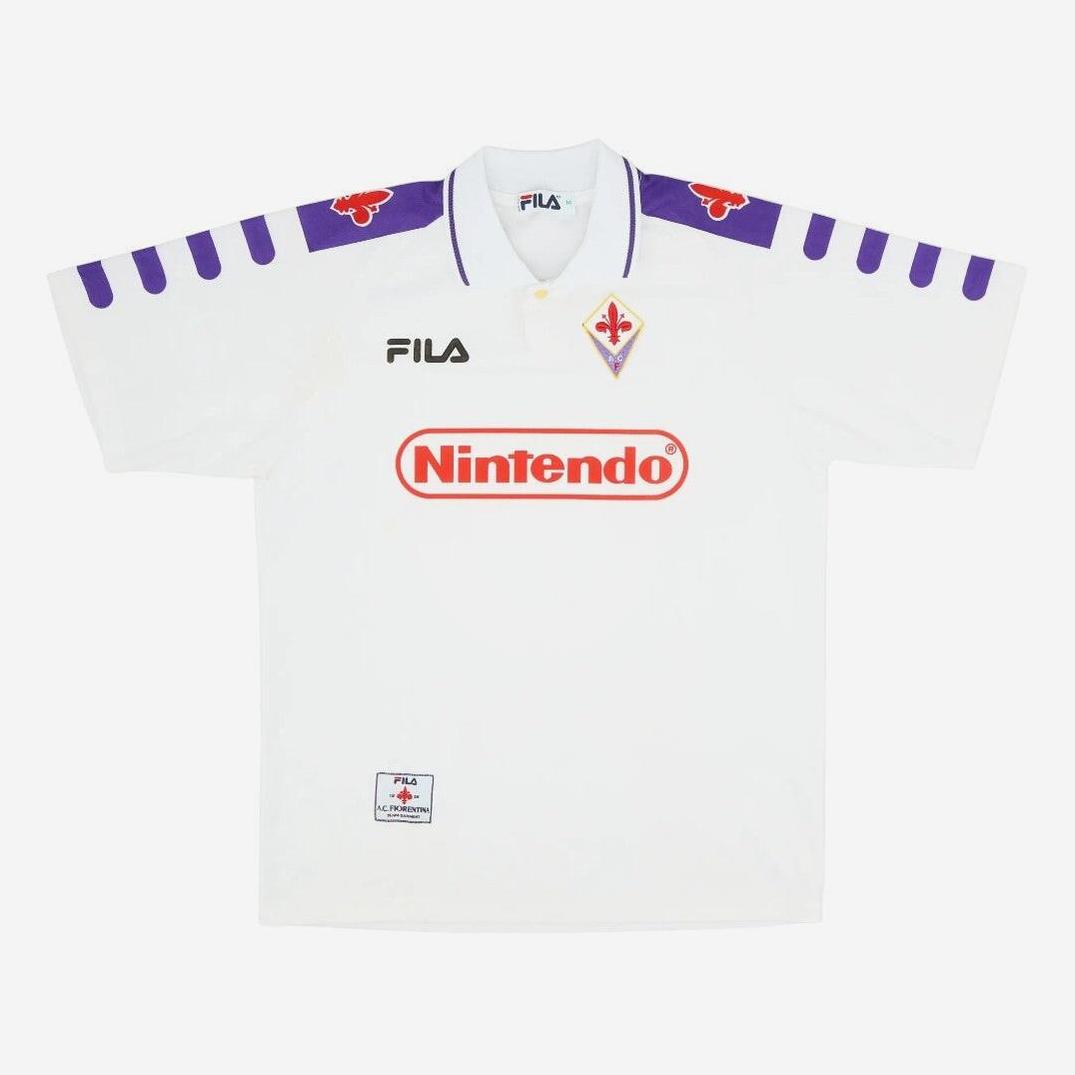 The Retro1999 Fiorentina 1998-99 Away Shirt is white with purple accents, FILA and Nintendo logos, club crest, purple patterns, and red fleur-de-lis on the shoulders—a classic Serie A era retro kit.