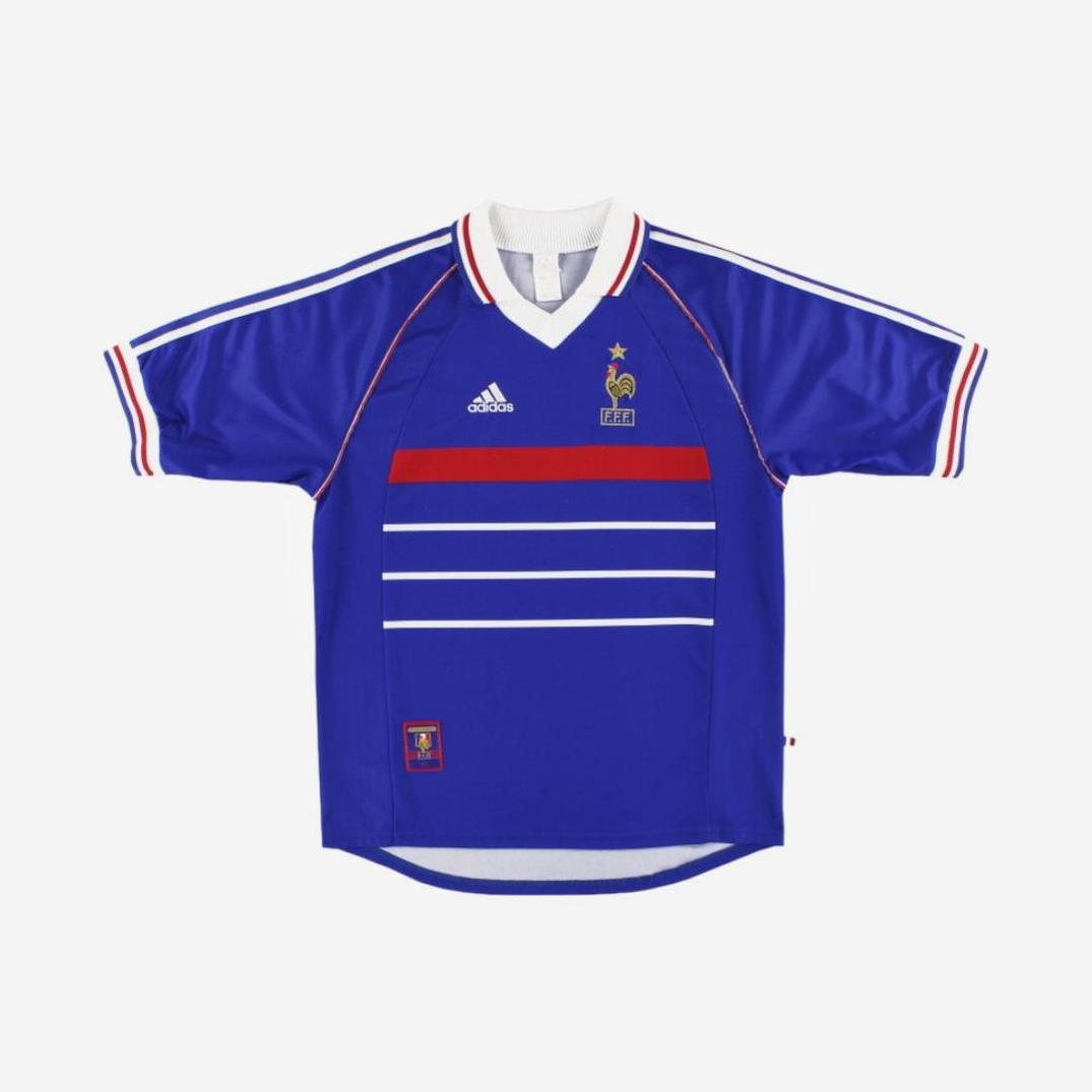 The France 1998 Home Shirt by Retro1999 features blue fabric with white and red accents, plus the classic gold rooster crest and a star—an iconic retro kit celebrating the French national teams World Cup victory.