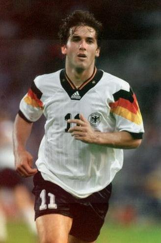A soccer player in the Retro1999 Germany 1992 Home Shirt, featuring bold black, red, and yellow stripes and number 11, sprints across the pitch, drawing admiration from football fans.