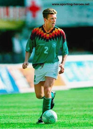 A male soccer player in a Retro1999 Germany 1994 Away Shirt, numbered 2, is running on a grassy field with a soccer ball at his feet.
