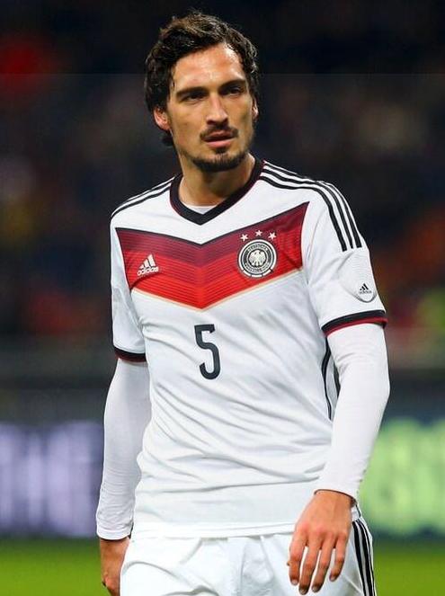 A male soccer player wears the Retro1999 Germany 2014 Home Shirt, featuring number 5 with white, red, and black accents, and stands on the field during a match.