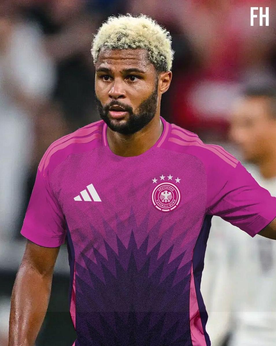 A male soccer player with blond curly hair and a trimmed beard wears the Retro1999 Germany 2024 Away Shirt, a bold purple and pink retro kit, featuring four stars and white Adidas logo, standing on the field during a match.