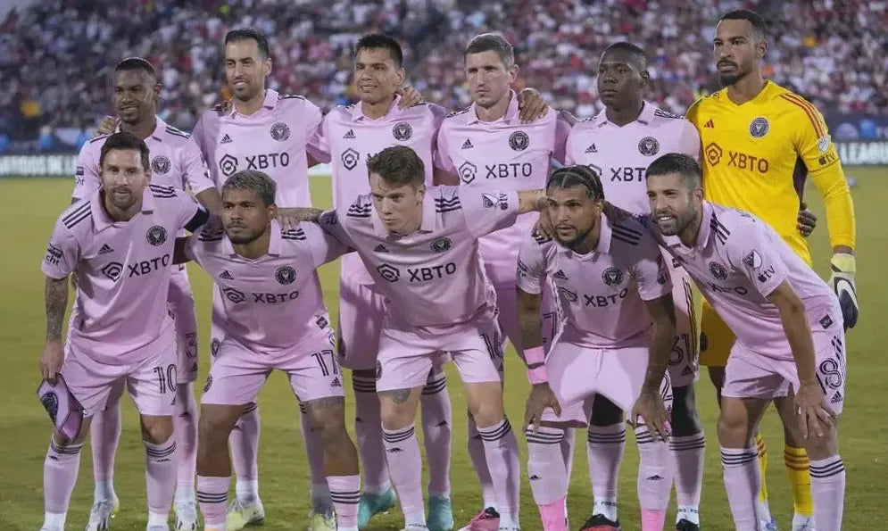 A soccer team wearing Retro1999 Inter Miami 2023/24 Home Shirts poses on the field before an MLS match, with ten players in two rows and a crowded stadium behind them.