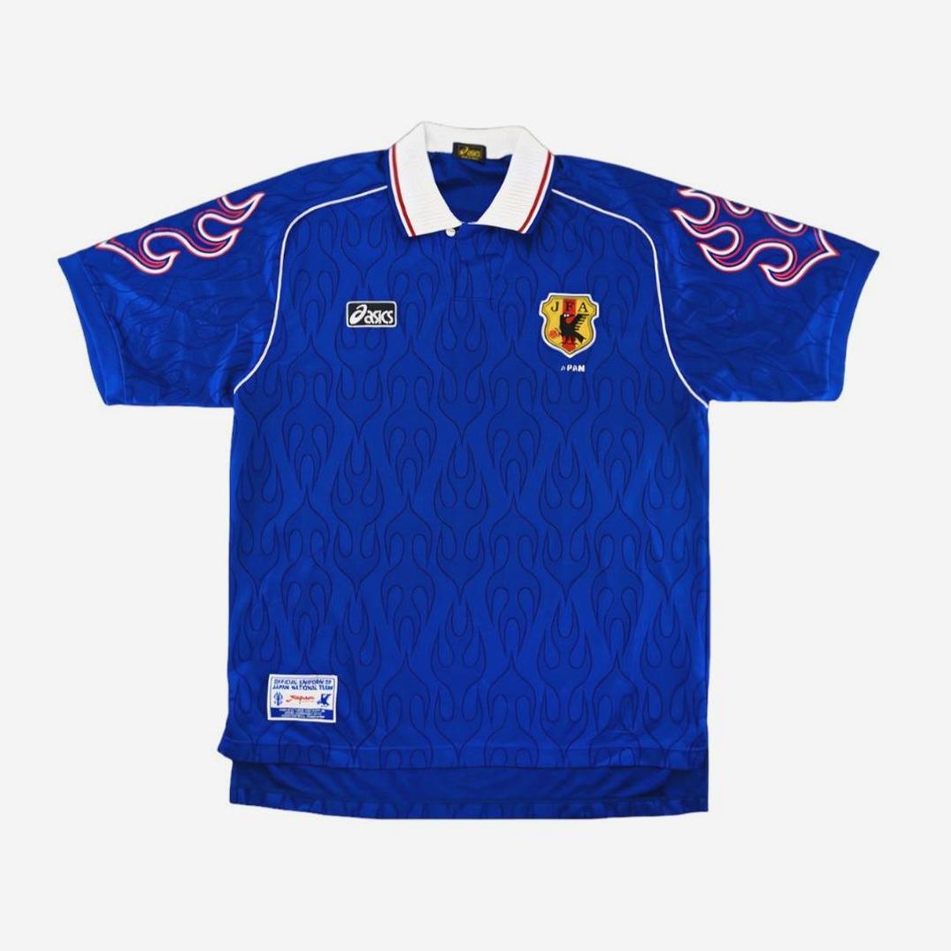 The Retro1999 Japan 1998 Home Shirt features blue fabric, flame patterns, a white collar, Asics logo, and the team crest. Its sleeves have standout red and white flames—a classic piece of Japanese football history.