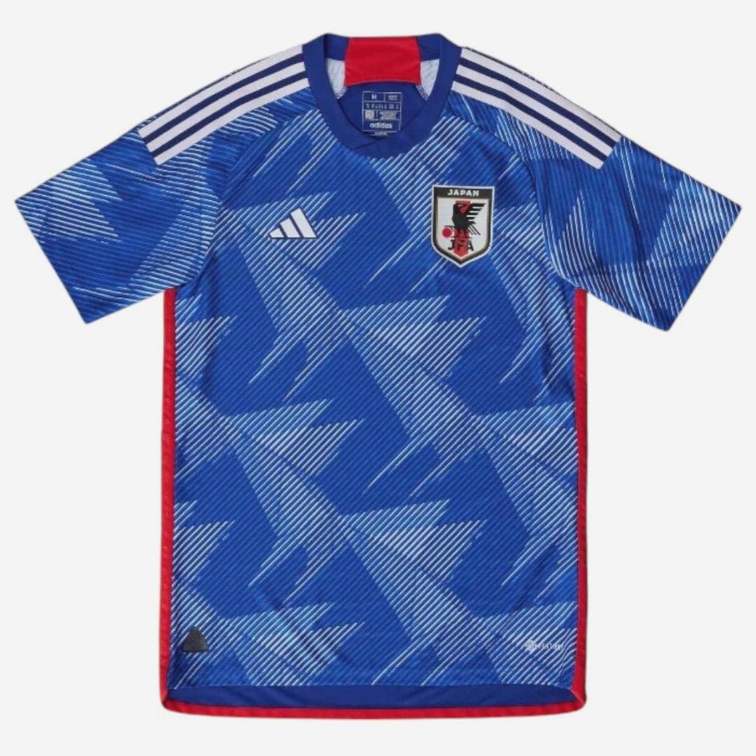 The Retro1999 Japan 2022 Home Shirt is blue with white shoulder stripes, a geometric design, the Japanese team badge on the chest, red side trim, and offers a modern update to a classic style.
