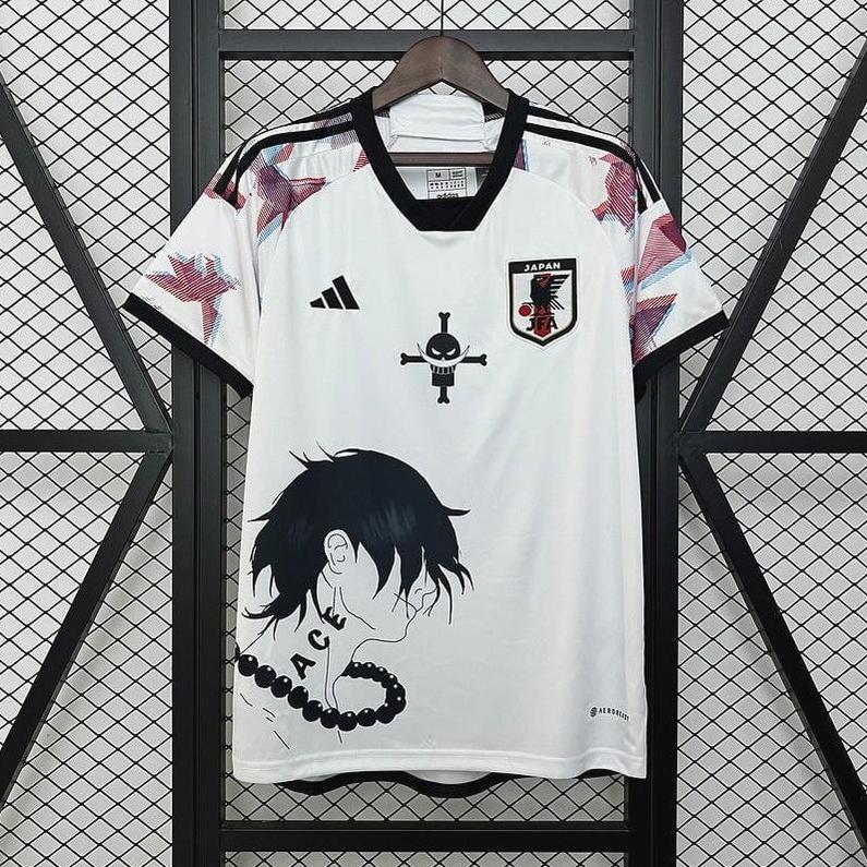 A Retro1999 Japan 2024 Special Edition Shirt featuring black and red shoulder patterns, an anime-style front graphic, and a national team patch on the left chest, displayed on a wooden hanger in front of a wire grid.
