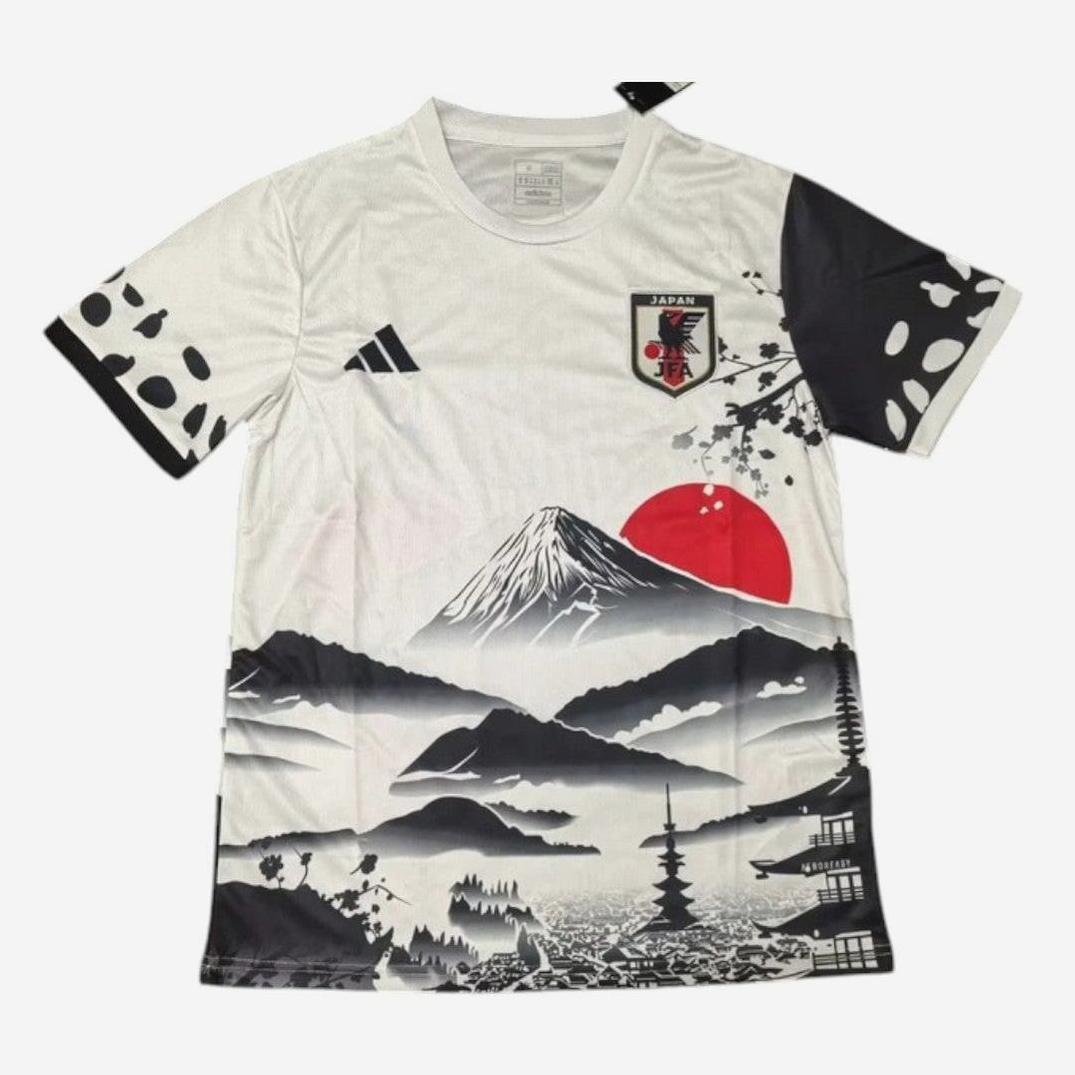 The Retro1999 Japan 2025-26 Special Edition Shirt is a white jersey with a black and gray Mount Fuji illustration, red sun, cherry blossoms, Japanese buildings, the Japan football crest on the chest, and black sleeve patterns.