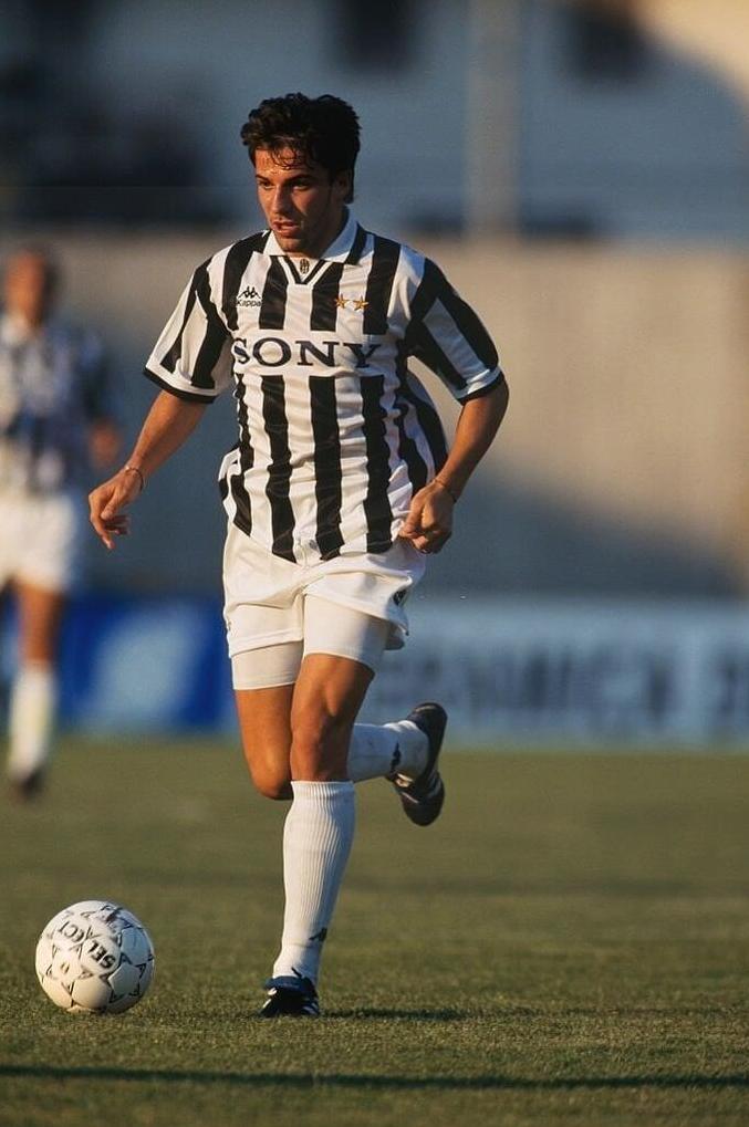 A soccer player, focused like a Serie A star, dribbles a white ball on grass while wearing the Retro1999 Juventus 1995-97 Home Shirt with SONY across the front.