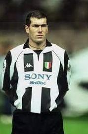 A male soccer player stands on the field with his hands behind his back, wearing the Juventus 1997-98 Home Shirt by Retro1999—an authentic piece featuring the classic Sony sponsor logo and timeless club heritage.