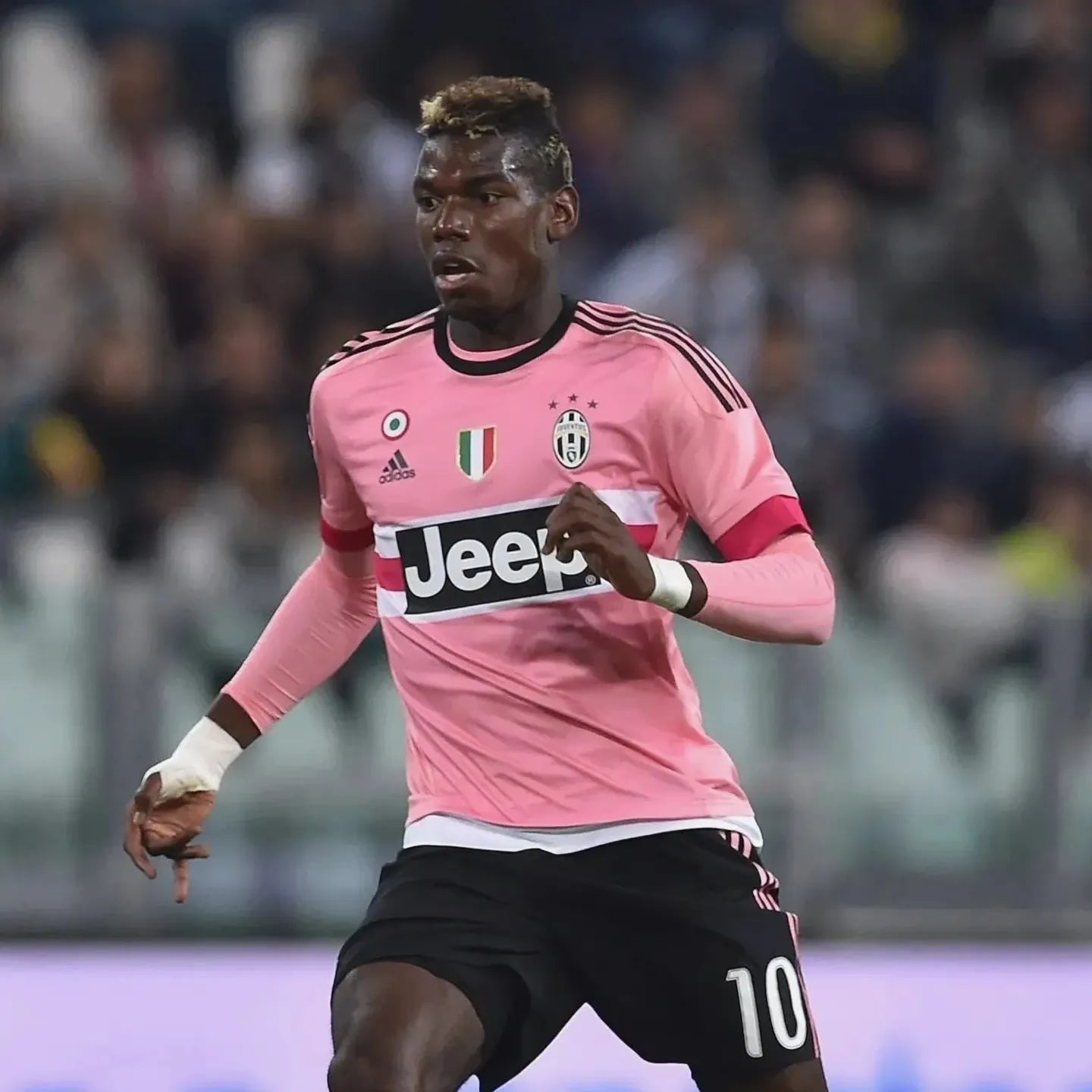 A soccer player in a pink My Store Juventus 2015-16 Away Shirt with number 10 and Jeep sponsor is running on the field for the Serie A club, with blurred spectators in the background.