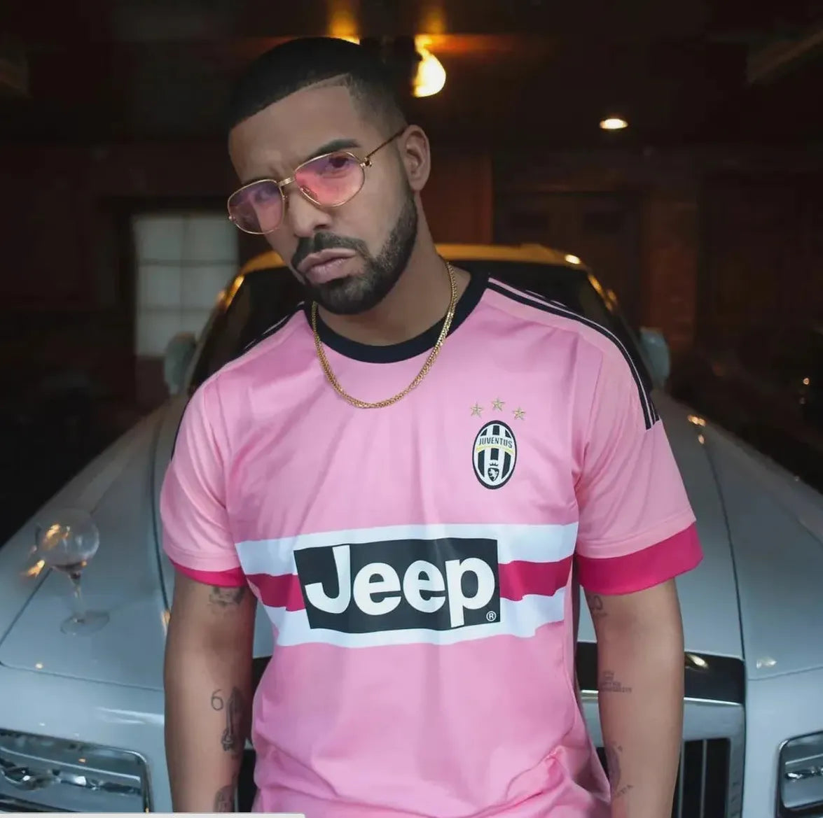 A bearded man in pink sunglasses sports the My Store Juventus 2015-16 Away Shirt, featuring Jeep branding, as he stands by a white car with a wine glass on the hood, proudly showing support for his favorite club.
