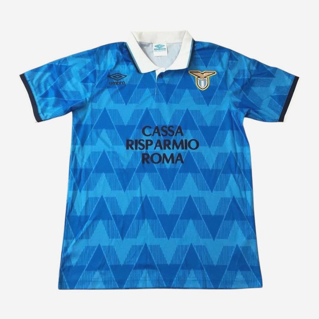 The Retro1999 Lazio 1989-91 Home Shirt features a blue geometric pattern, white collar, black trim, Cassa Risparmio Roma sponsor, Umbro logo, and club badge—an iconic piece from the Serie A era.