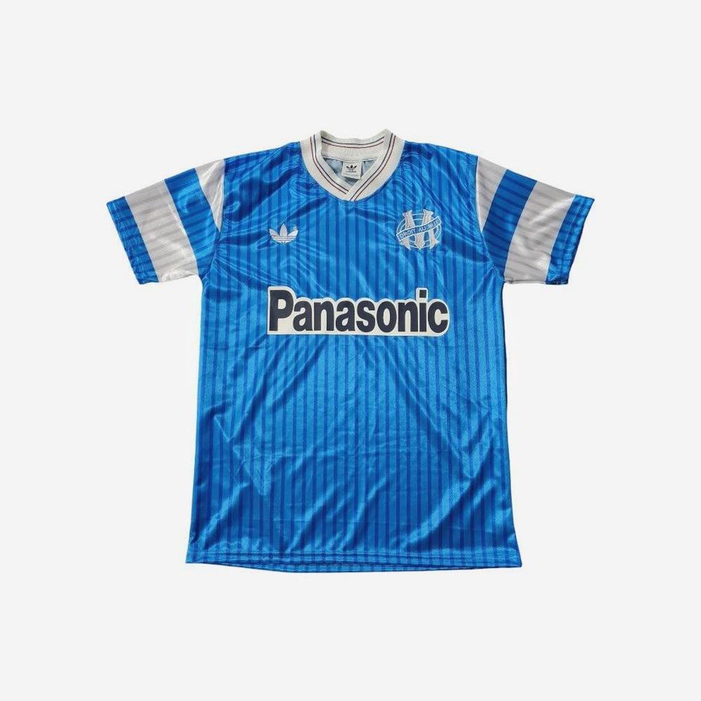The Retro1999 Marseille 1990-91 Away Shirt is a blue and silver short-sleeve jersey with subtle vertical stripes, Panasonic sponsor logo, and a white collar with blue trim—ideal for classic retro kit fans.