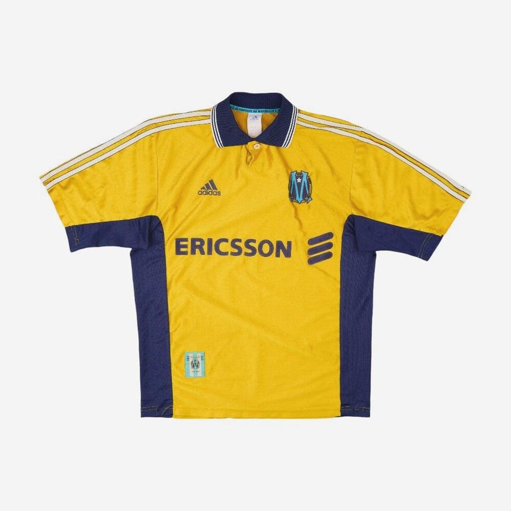 The Marseille 1998-99 Third Shirt by Retro1999 features yellow and navy blue colors, white shoulder stripes, an Ericsson sponsor logo, and a blue-yellow crest—a classic Ligue 1 jersey for football fans.