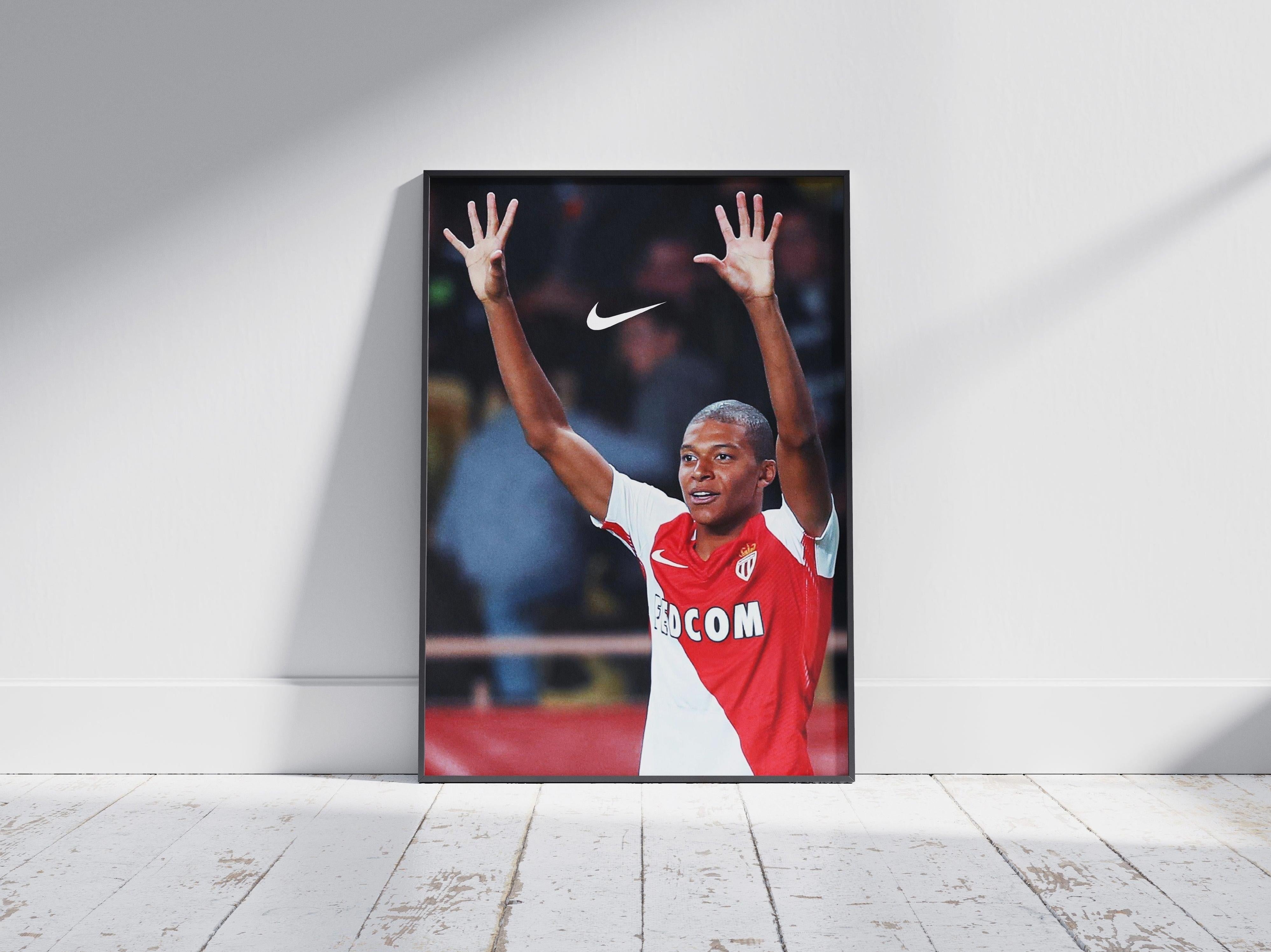 The Retro1999 Mbappe x AS Monaco Poster features Kylian Mbappe in a red and white jersey with arms raised, standing against a wall on a white wooden floor. The Nike logo is displayed above him.