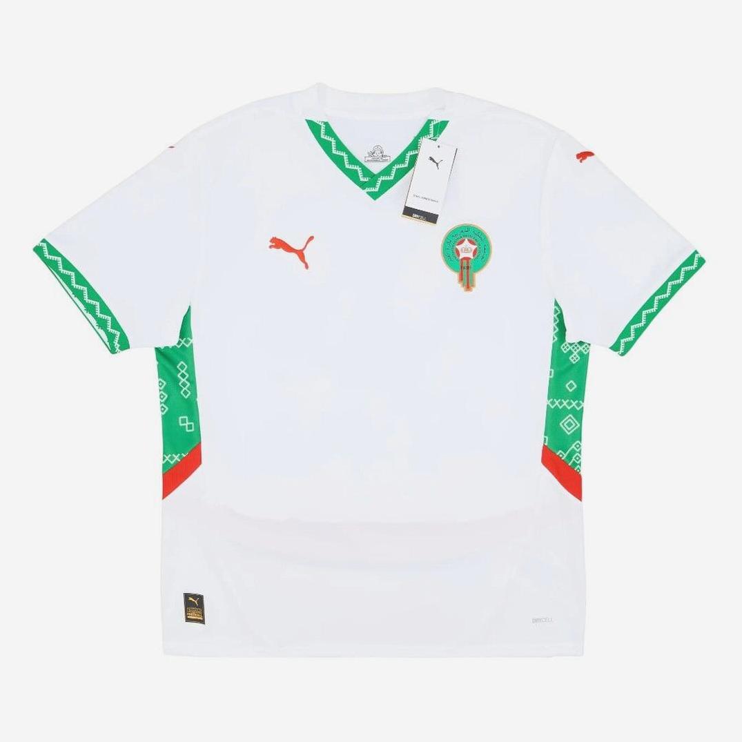 The Morocco 2024-25 Away Shirt by Retro1999 is a white retro kit with green geometric sleeve and collar patterns, red accents, and the Moroccan football badge. Tags are attached to the collar—ideal for national team supporters.