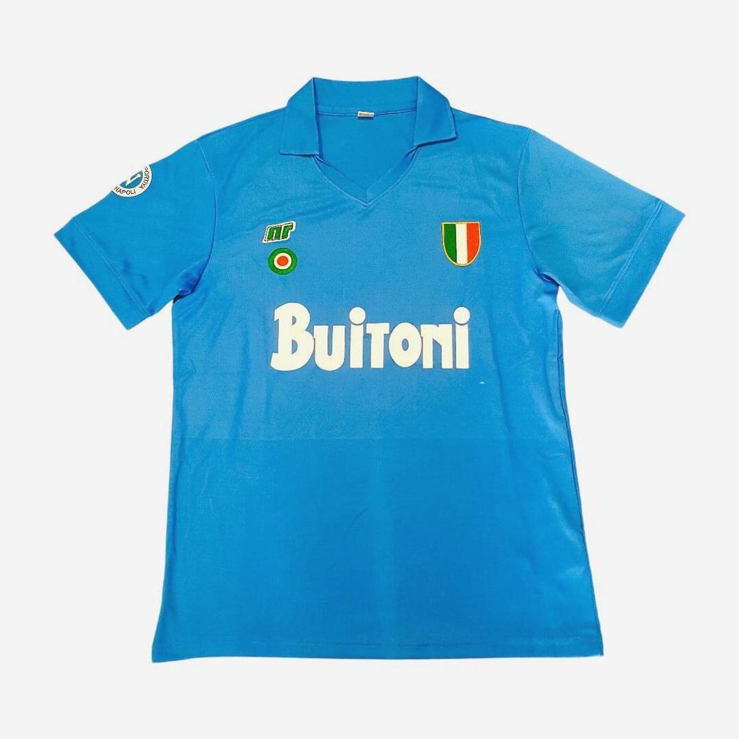 The Retro1999 Napoli 1987-88 Home Shirt is blue with Buitoni in white, a green, white, and red chest shield, right sleeve patch, classic collar, and short sleeves.