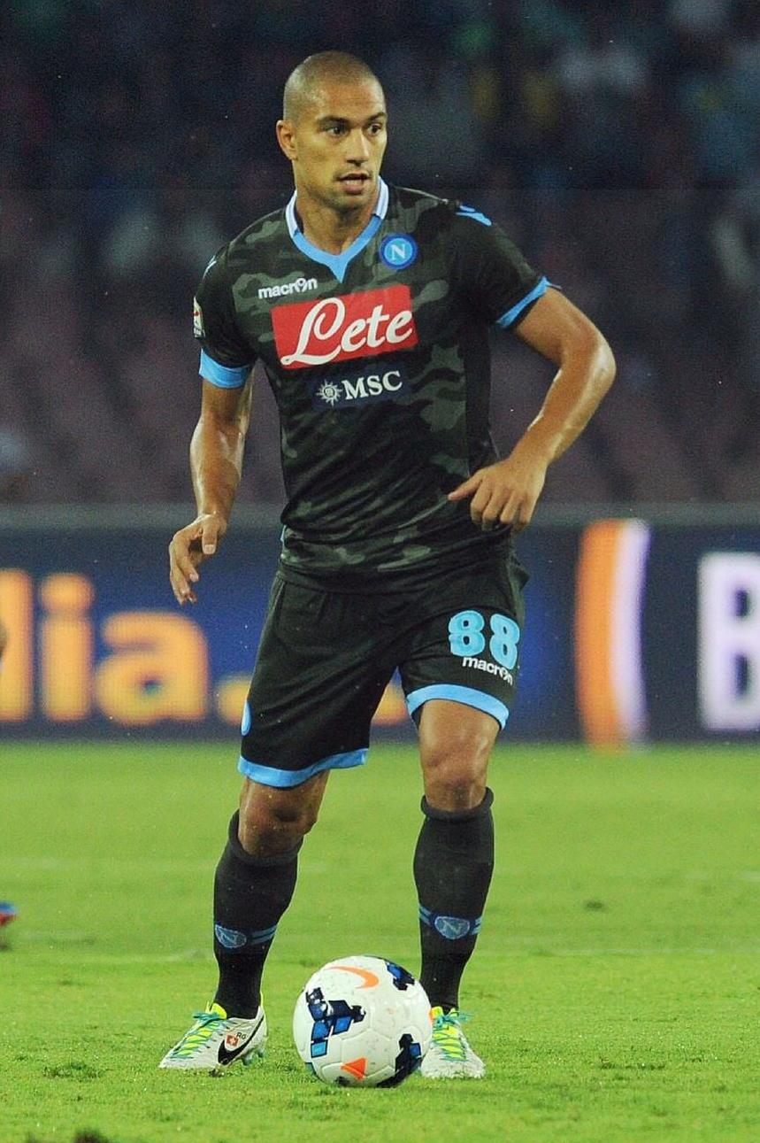 A soccer player in the Retro1999 Napoli 2013-14 Away Shirt, number 88, controls the ball on a grassy field during a match.