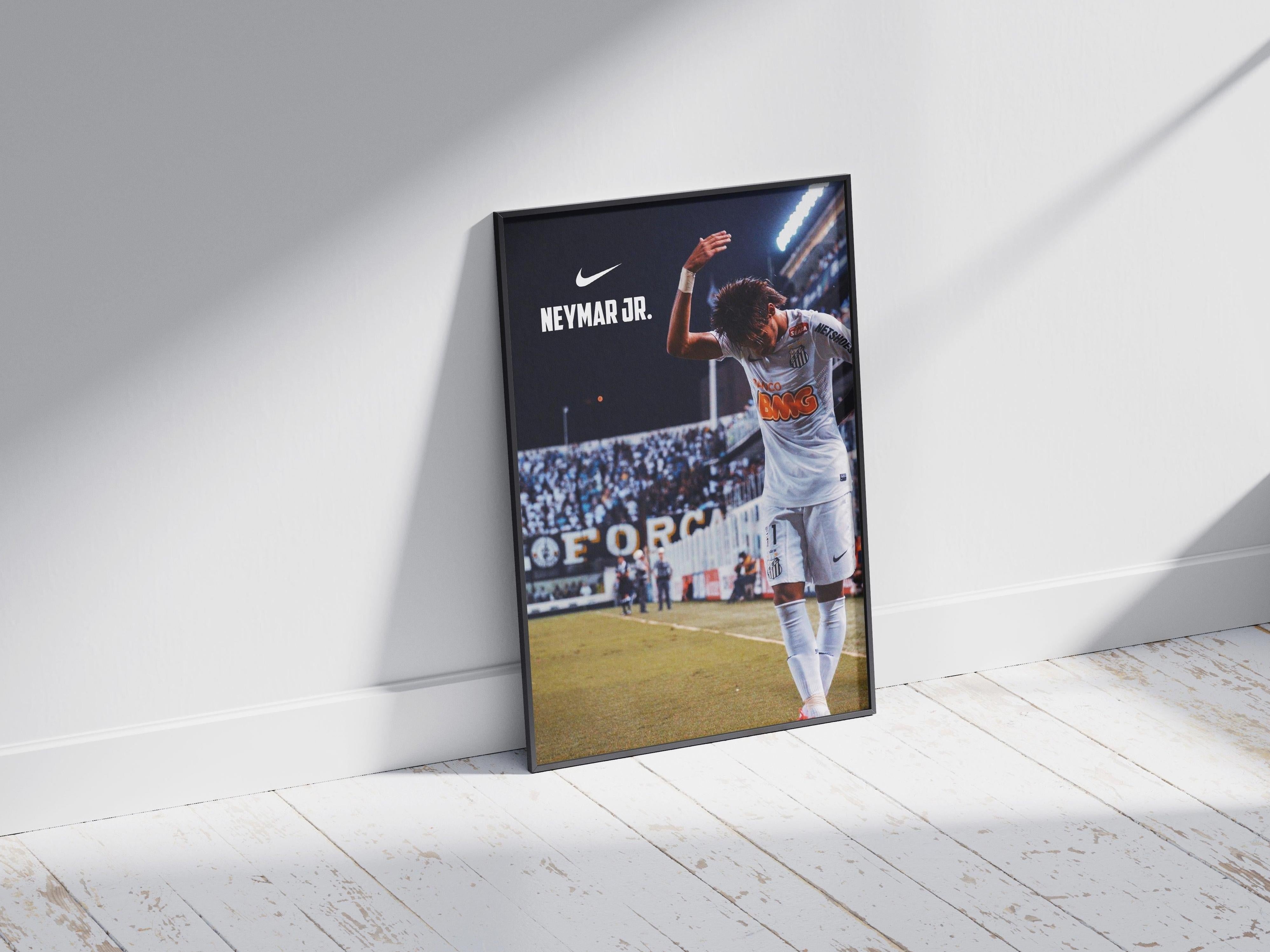 The Retro1999 Neymar Jr. x Santos Poster is a framed photo showing the soccer star in a white kit raising his arm on the field, with Nike and Neymar Jr. text above—ideal football memorabilia for fans, displayed on a sunlit wooden floor.
