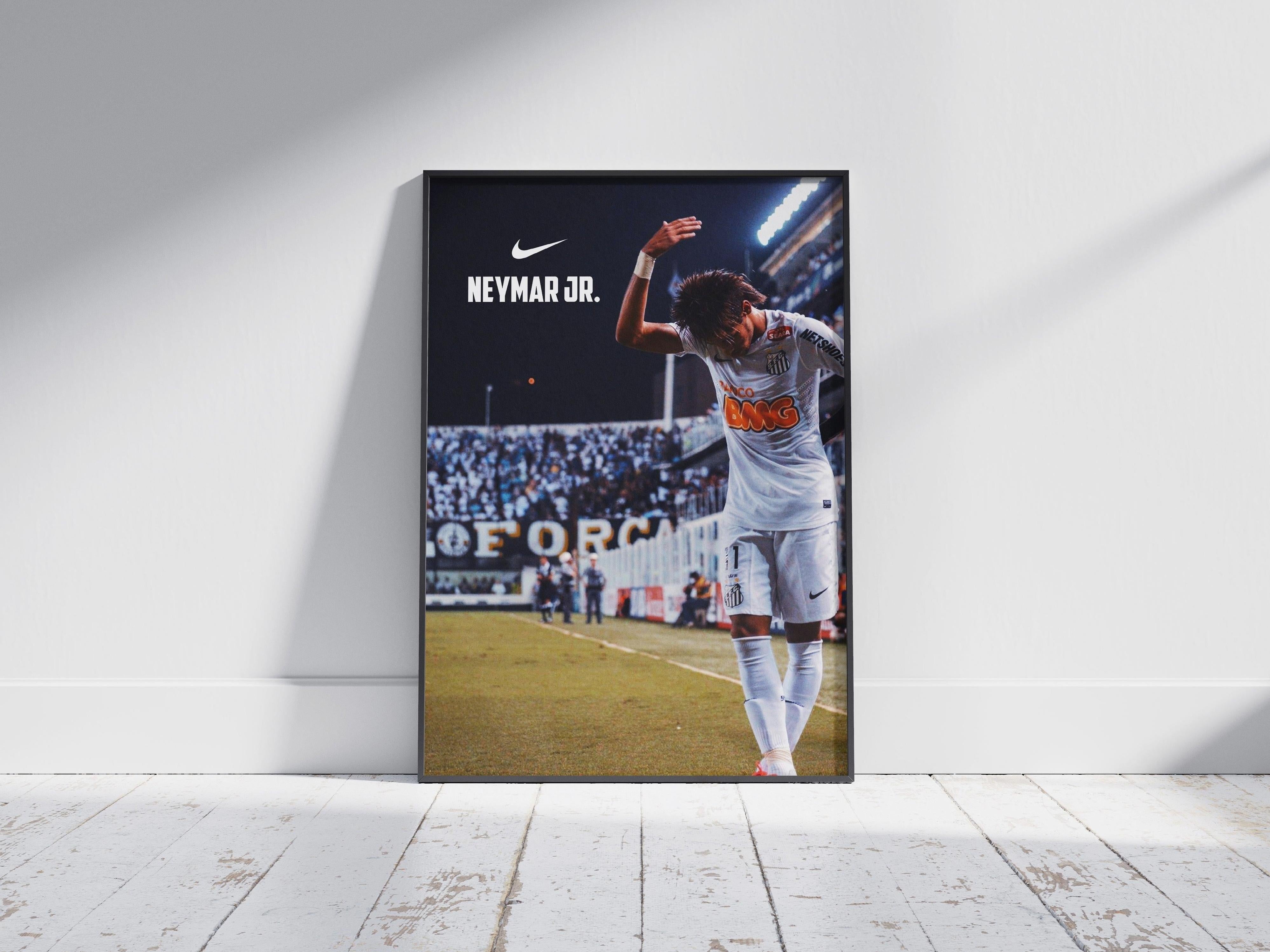 The Neymar Jr. x Santos Poster by Retro1999 shows the soccer star in a white kit celebrating on the field, with NIKE and NEYMAR JR. text above—ideal football memorabilia for fans, displayed against a white wall on a wooden floor.