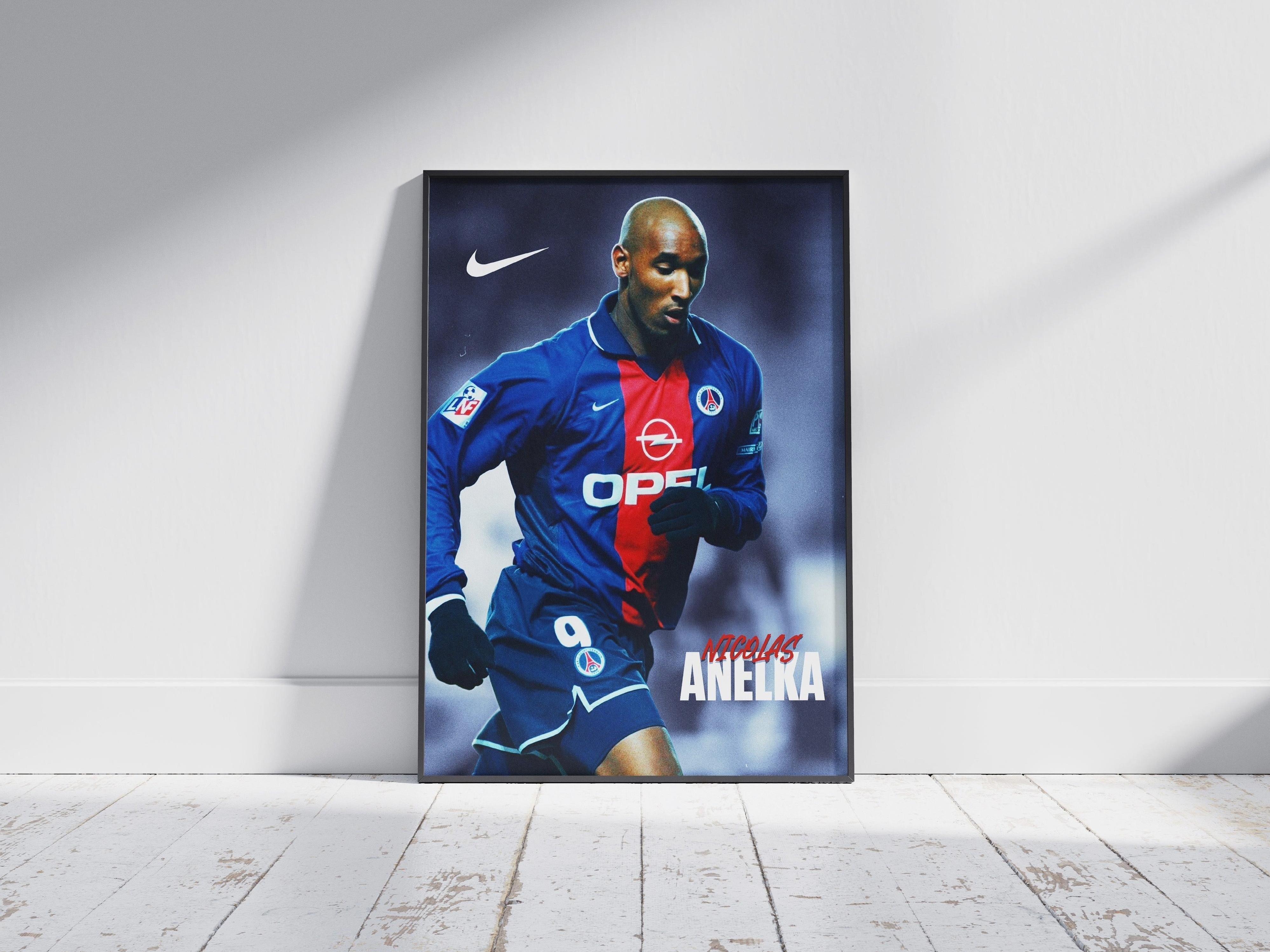 A framed Nicolas Anelka PSG Poster from Retro1999 lies on a wooden floor, showing Anelka in a blue and red kit with Opel and Nike logos as he sprints with the ball—his name stands out at the bottom.