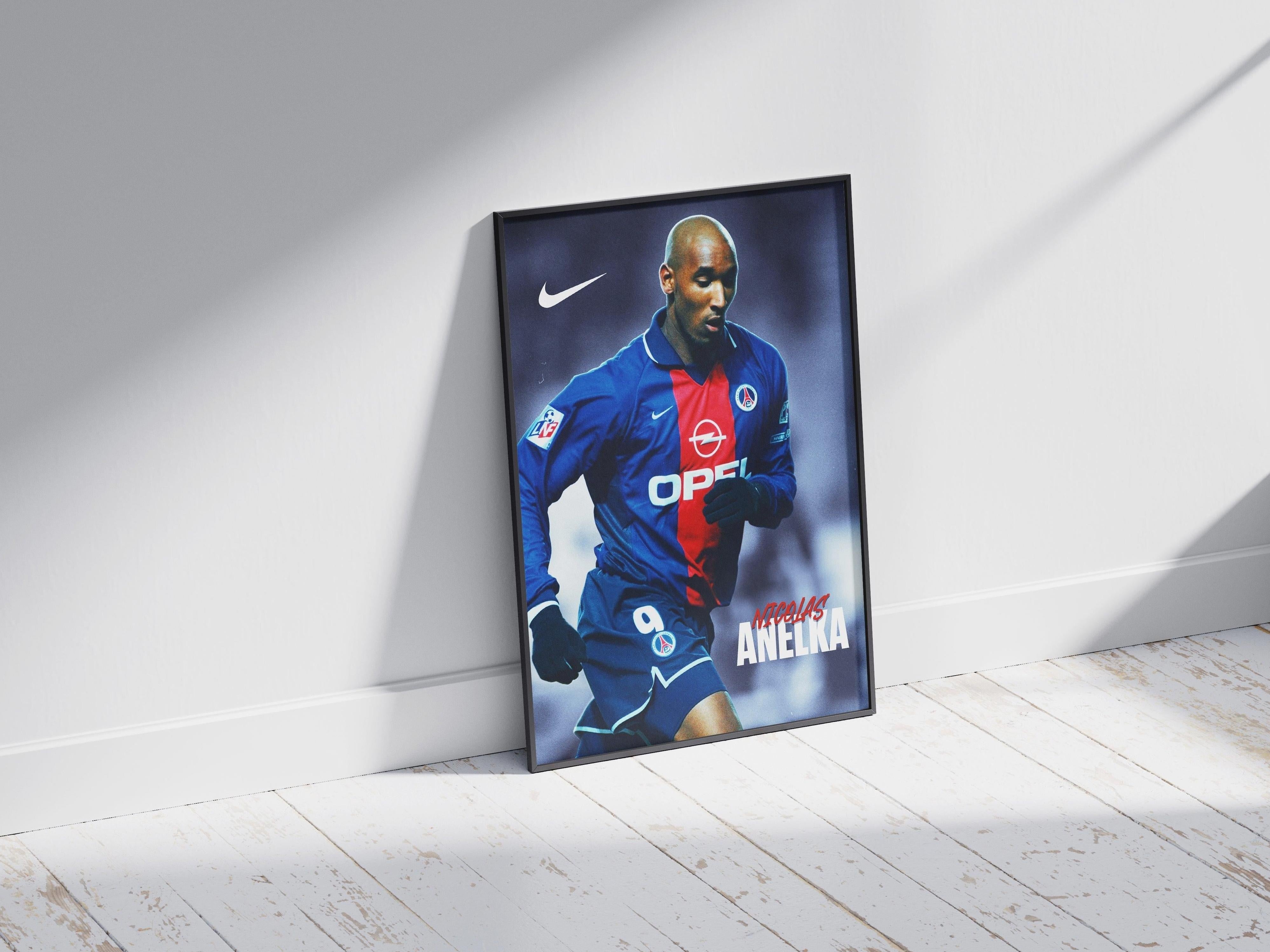 The Retro1999 Nicolas Anelka PSG Poster, showcasing the football star in a blue and red jersey, leans against a white wall on a sunlit wooden floor—ideal for soccer fans and collectors.