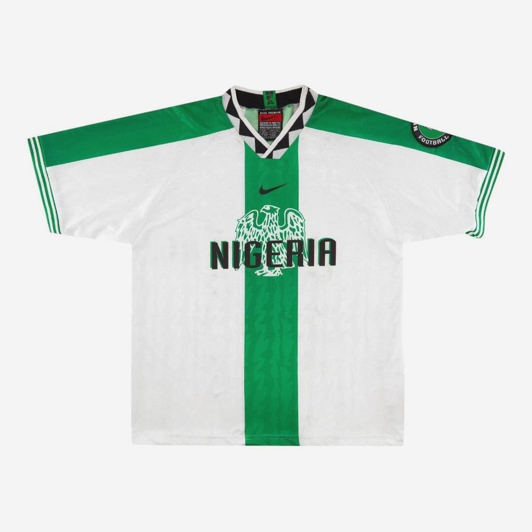 The Retro1999 Nigeria 1996 Away Shirt features a vintage white design with a bold green stripe, black eagle crest, NIGERIA text, green shoulder stripes, Nike logo, and sleeve badge—a classic retro kit for Nigerian football fans.
