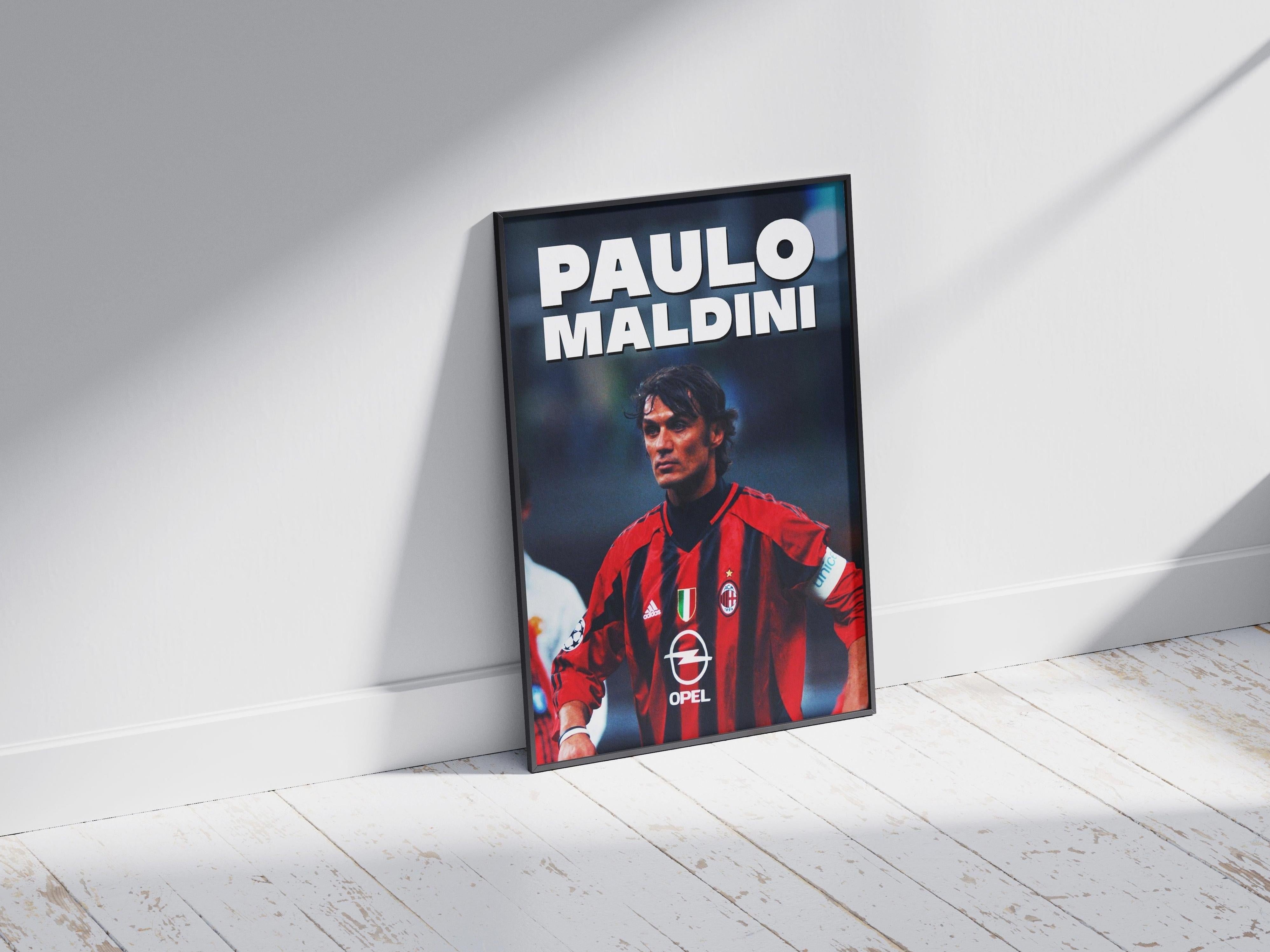 The Retro1999 Paolo Maldini AC Milan Poster features the football legend in a red and black jersey, with “PAOLO MALDINI” in bold white letters above. It leans against a white wall, bringing iconic football history to your space.