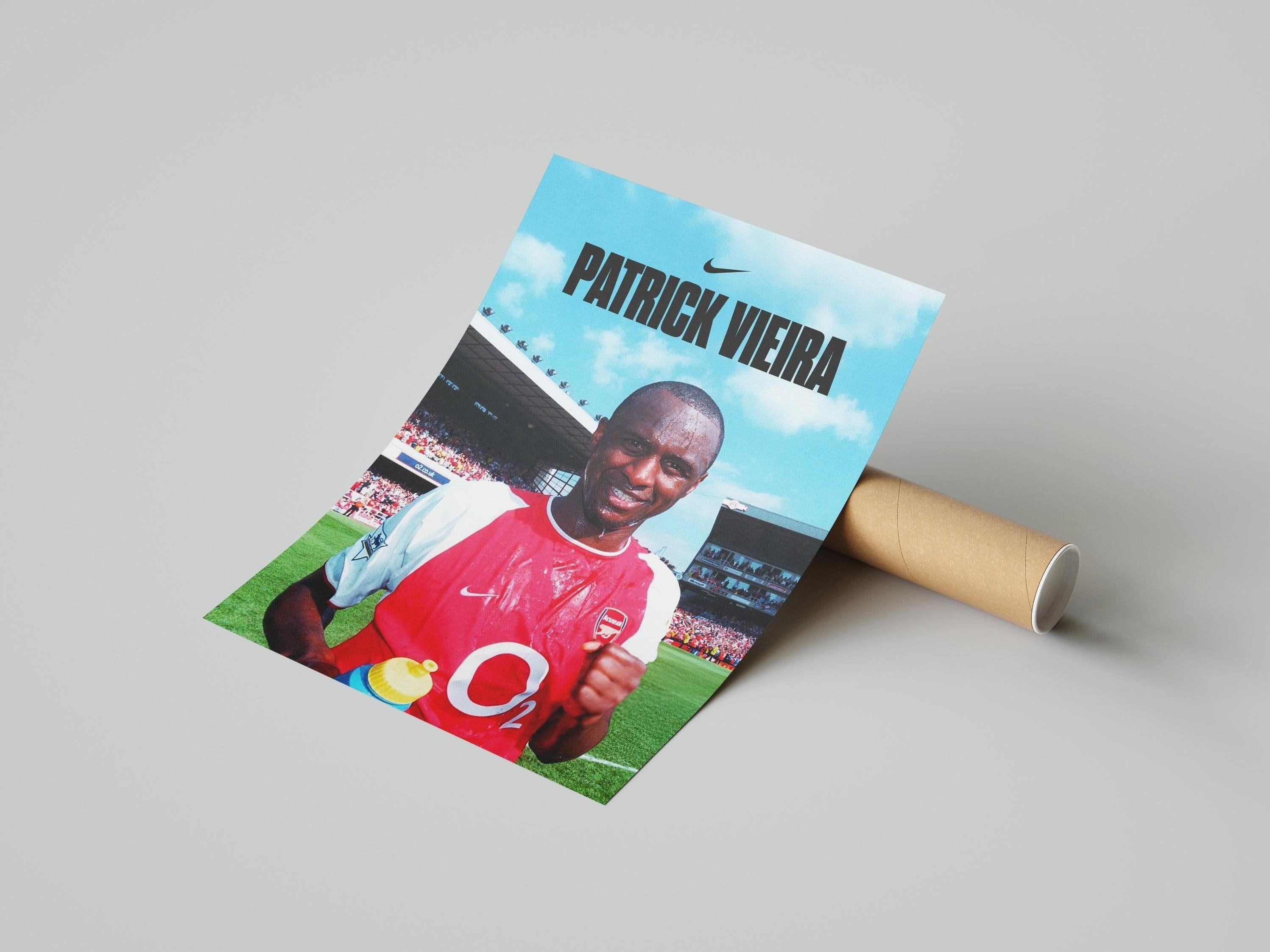 The Patrick Vieira x Arsenal Poster by Retro1999 shows Vieira in a Premier League victory, trophy in hand and iconic jersey, with a stadium backdrop. “PATRICK VIEIRA” and the Nike logo appear at the top. Poster is partially rolled next to its tube.