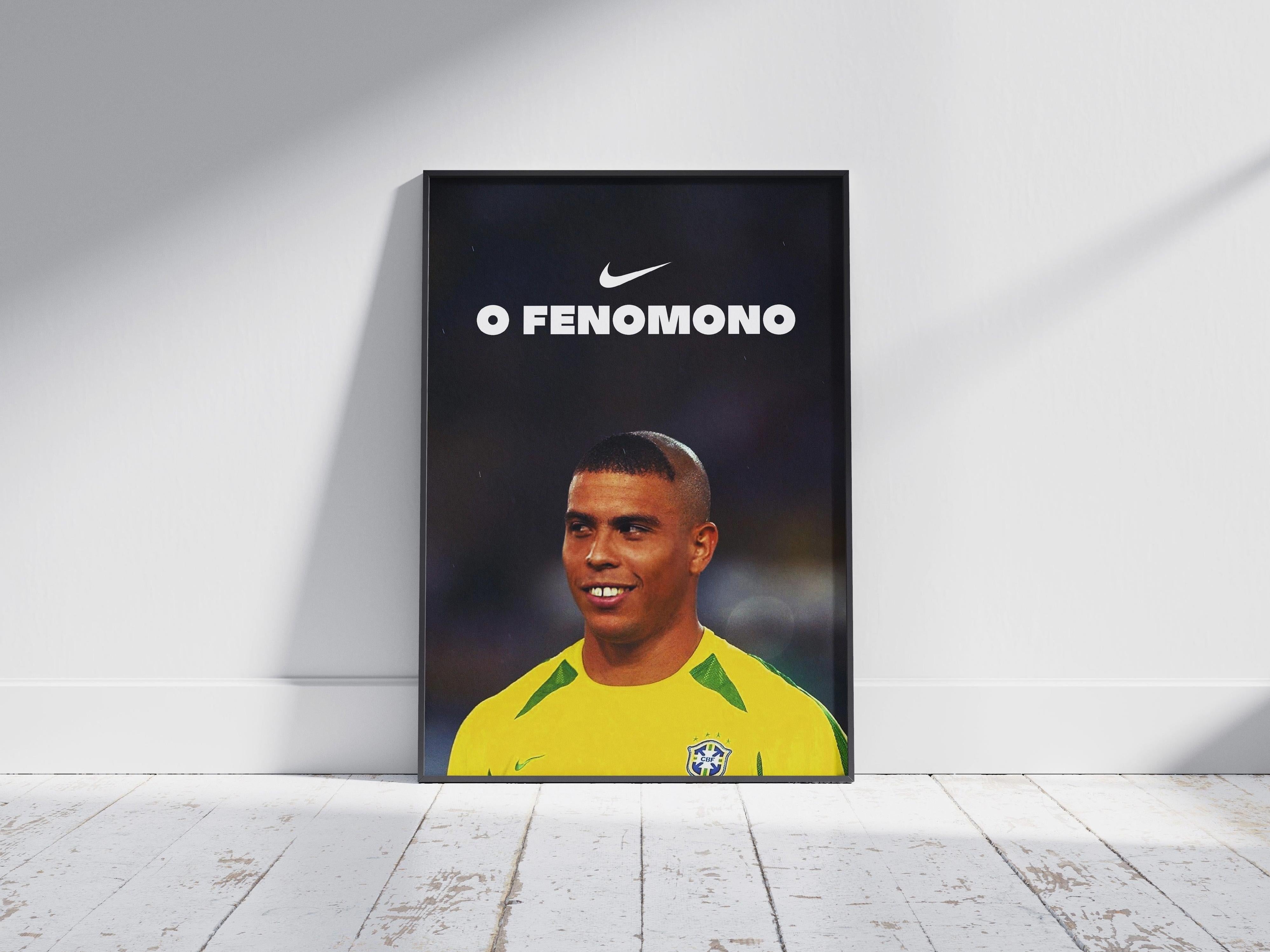 The Retro1999 R9 O Fenômeno Poster shows a smiling Ronaldo in Brazil’s yellow Nike jersey with O FENOMENO text, celebrating the 2002 World Cup, framed and set on a white wooden floor against a white wall.