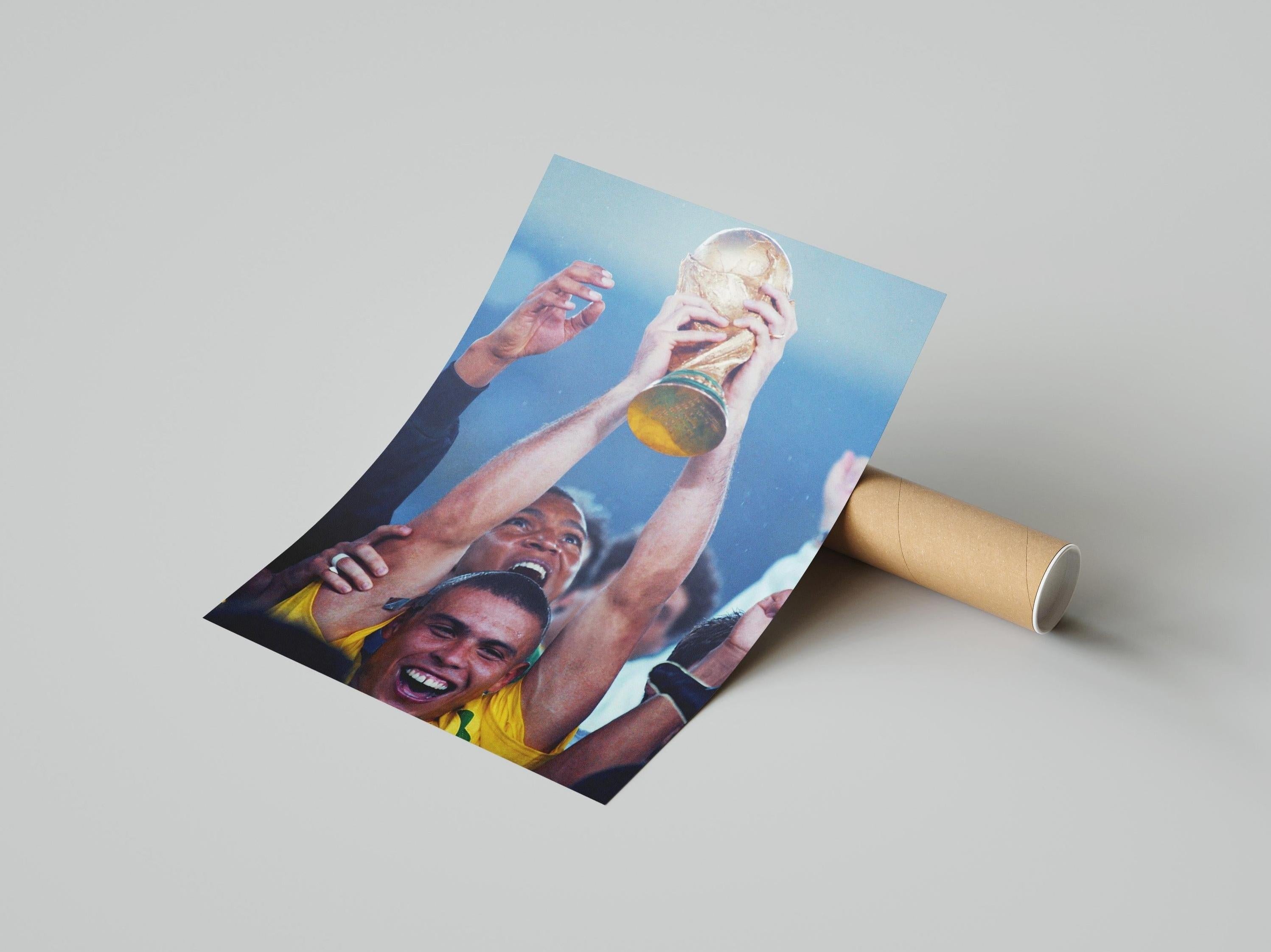 The R9 x World Cup Poster by Retro1999 shows soccer players, including Ronaldo, celebrating with the FIFA World Cup trophy; hands and smiling faces are visible as the print is partially unrolled next to a cardboard tube on a light background.
