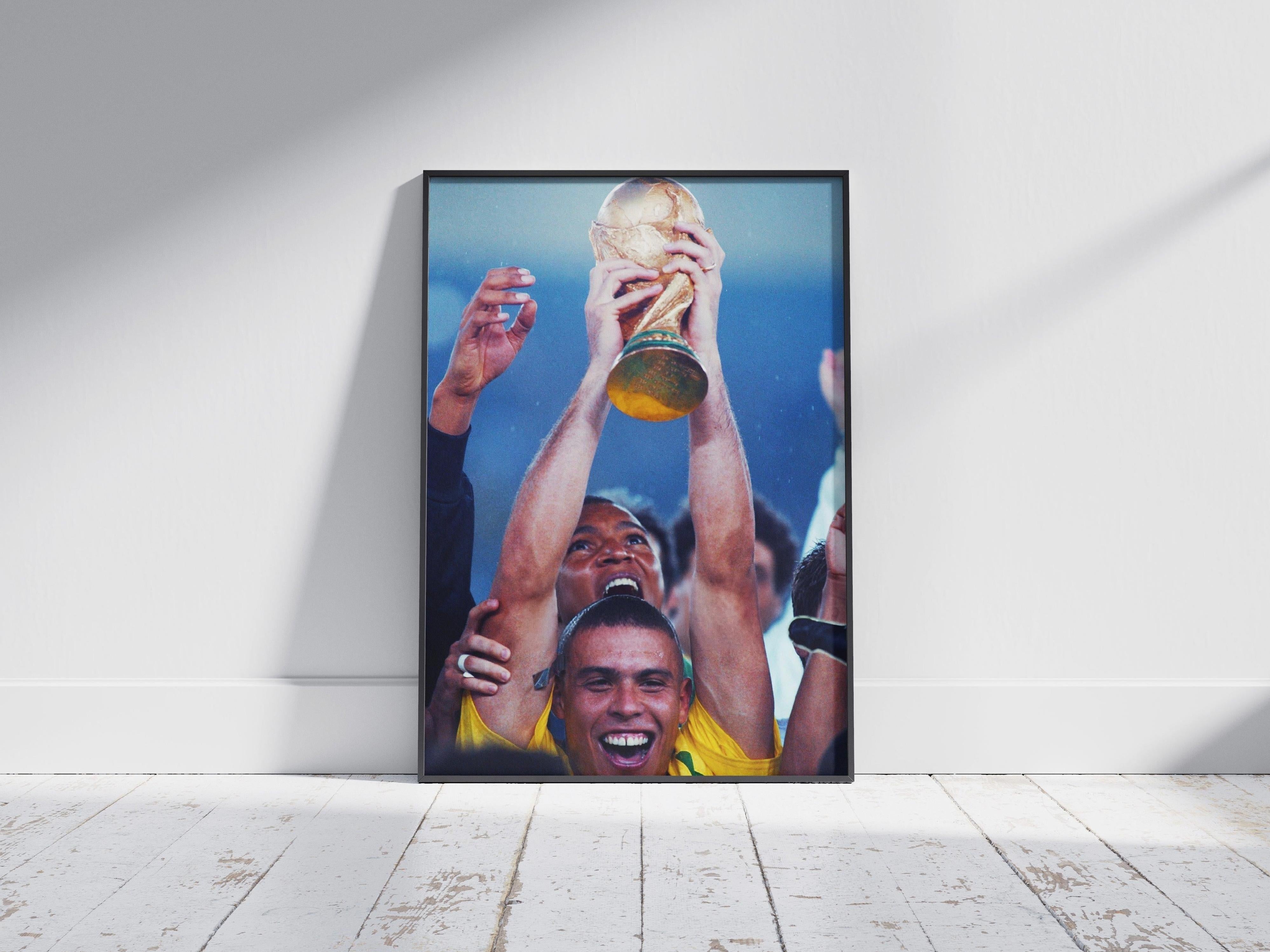 A framed photo on a sunlit wooden floor displays Retro1999s R9 x World Cup Poster, capturing a joyful soccer player hoisting a trophy amid celebrating teammates—a tribute to iconic Brazil Football Art.