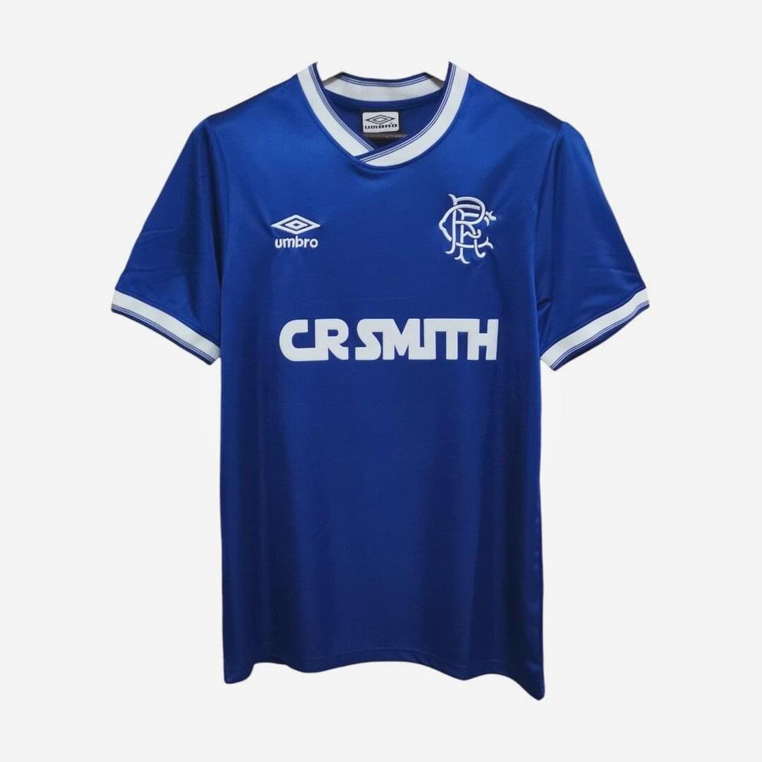 The Rangers F.C. 1984-87 Home Shirt by Retro1999 is a blue jersey with white trim, featuring the Umbro logo, club crest, and CR SMITH sponsor—ideal for football history fans and retro kit collectors.