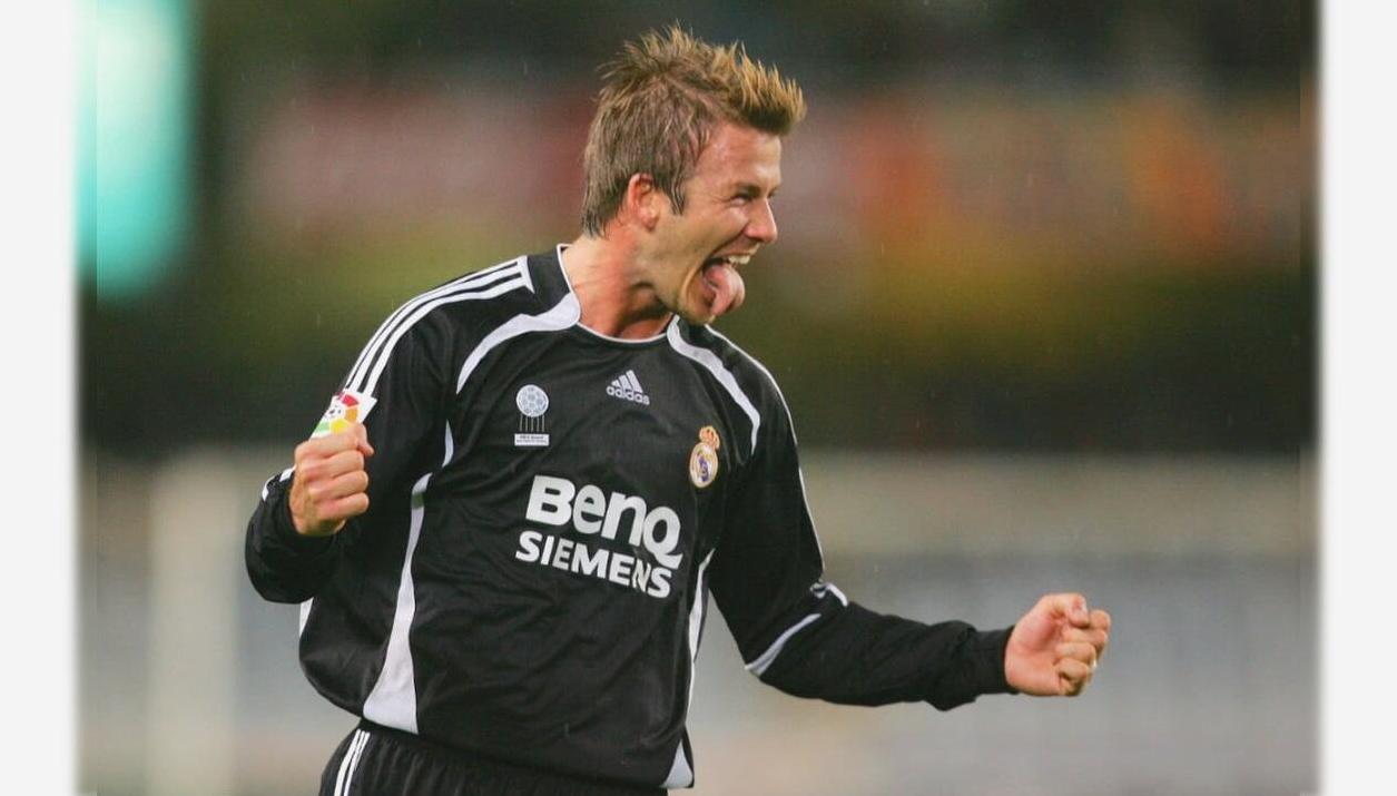 A soccer player in a Retro1999 Real Madrid 2006-07 Away Shirt celebrates passionately with clenched fist and tongue out during a match, chasing the La Liga title.