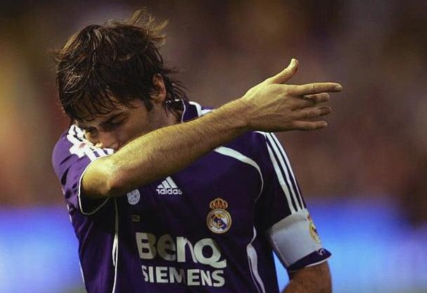 A soccer player wearing the Retro1999 Real Madrid 2006-07 Third Shirt and a captain’s armband wipes his face with his arm on the field, standing out against a blurred background that captivates football fans.