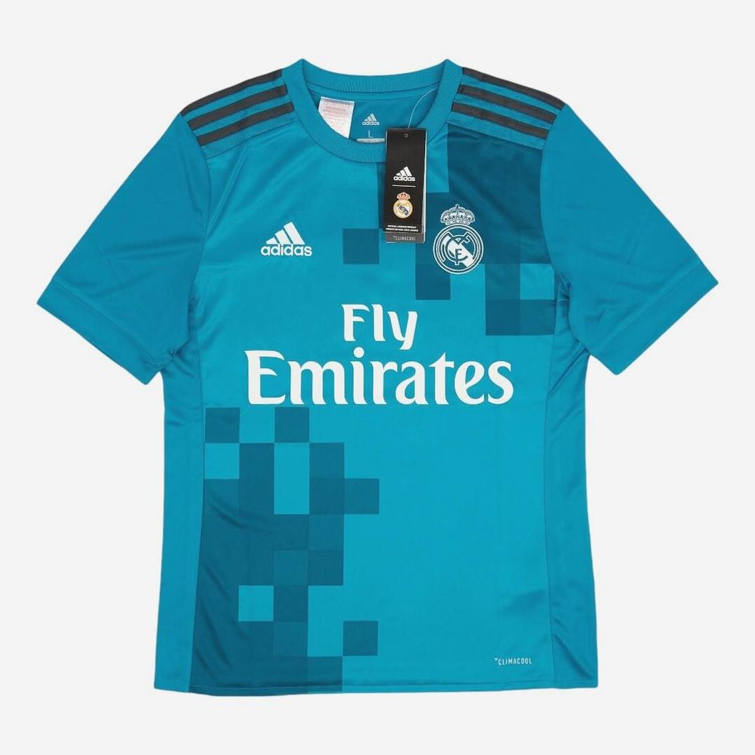 The Retro1999 Real Madrid 2017-18 Third Shirt is a teal short-sleeve La Liga jersey with a pixelated retro design, three dark shoulder stripes, and features Adidas and Fly Emirates logos plus a collar tag.