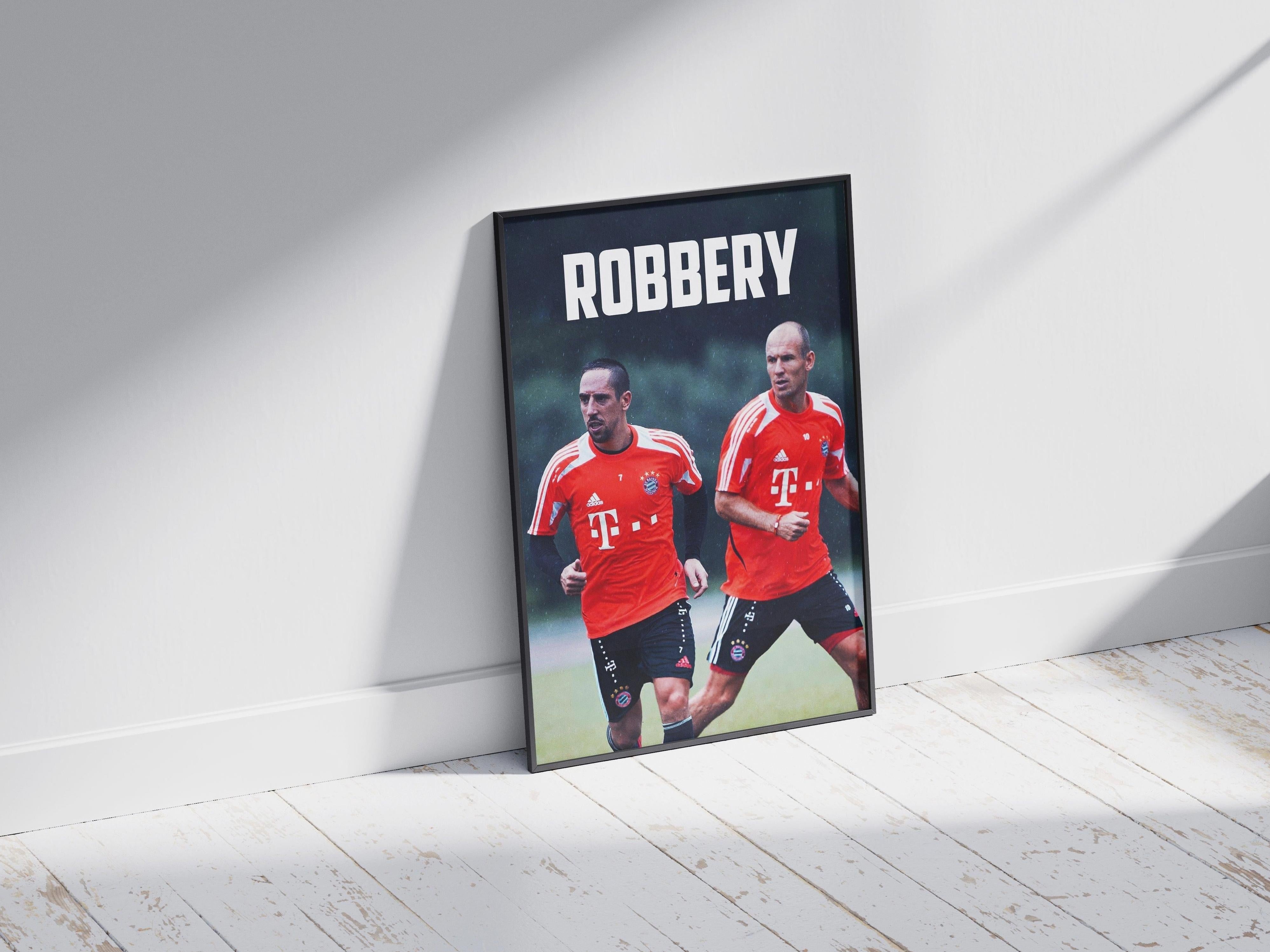 The Retro1999 Robben x Ribery ROBBERY poster features the Bayern Munich legends in red jerseys, running side by side under bold white ROBBERY text, shown framed and resting on a wooden floor.