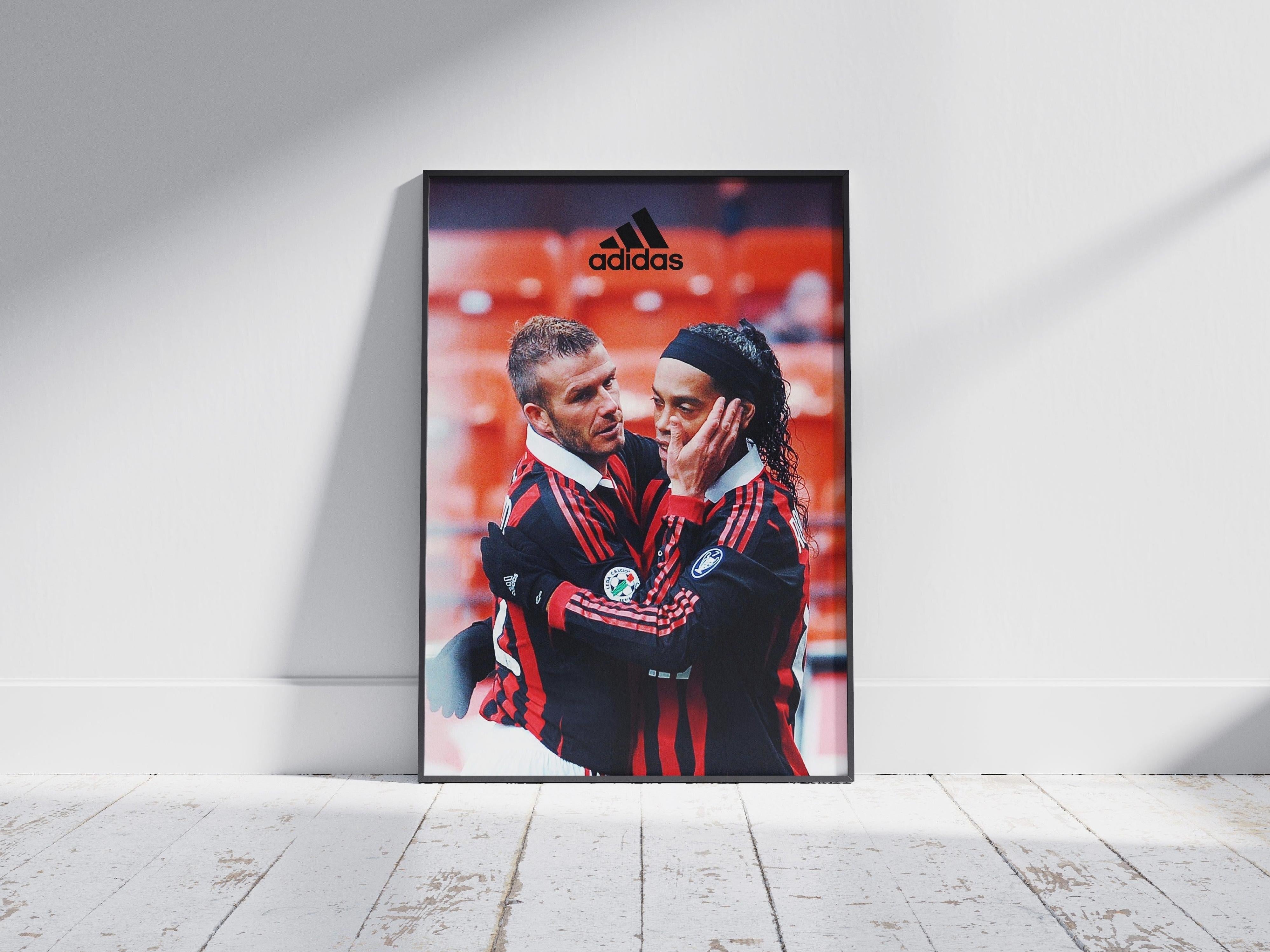 The Ronaldinho x David Beckham Poster by Retro1999 features two soccer stars in red and black jerseys, with one gently holding the other’s face—an iconic scene and unique football memorabilia, complete with a visible Adidas logo.